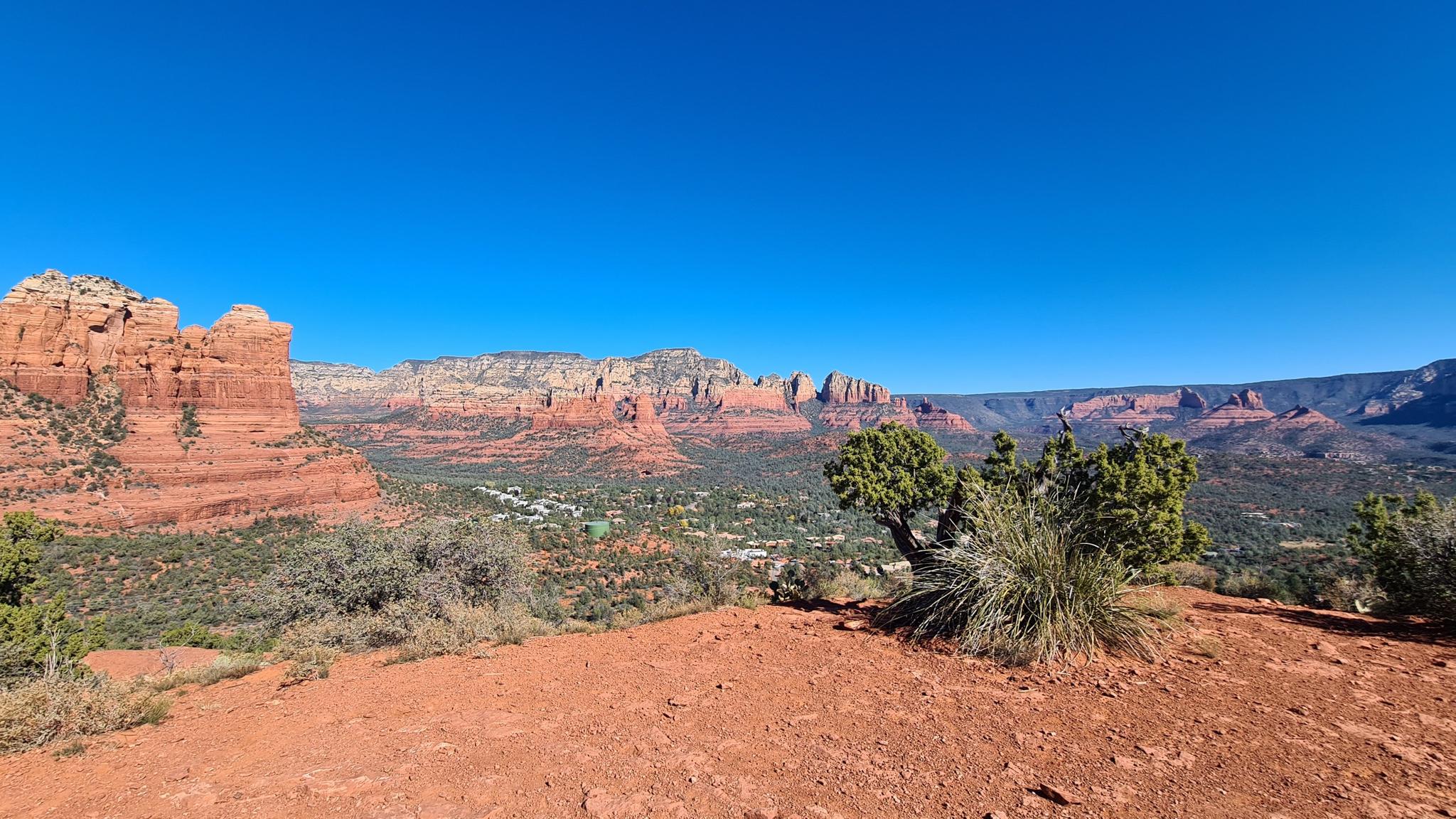 Red desert foreground with distant red rock formations under a clear blue sky.