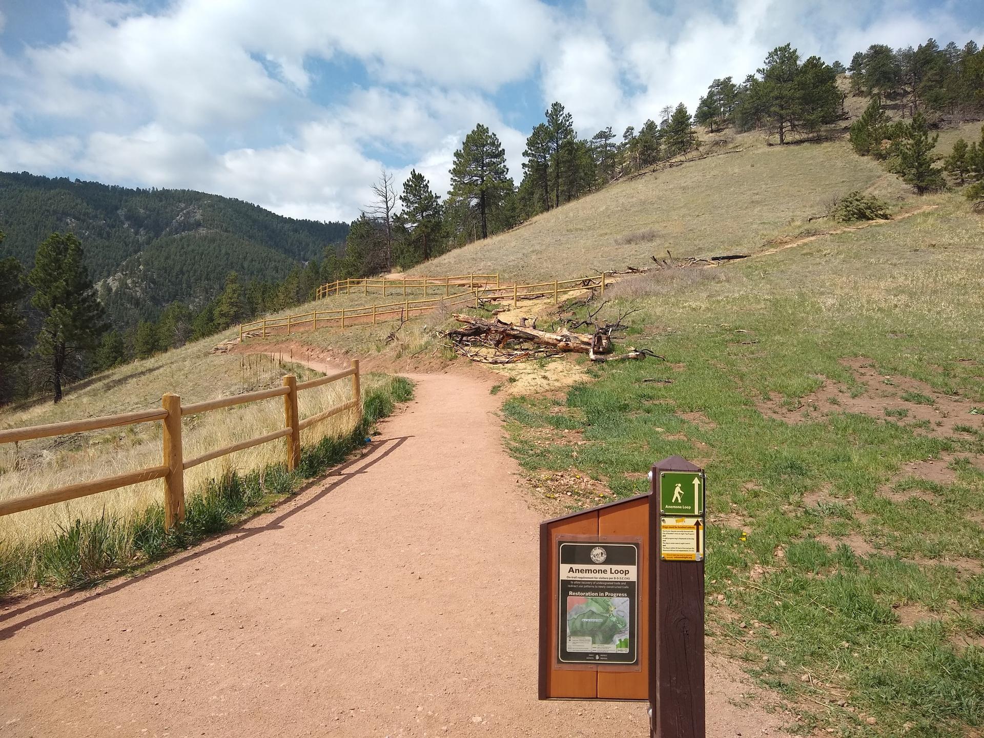 Dirt path with wooden fence leading uphill past a trail sign.