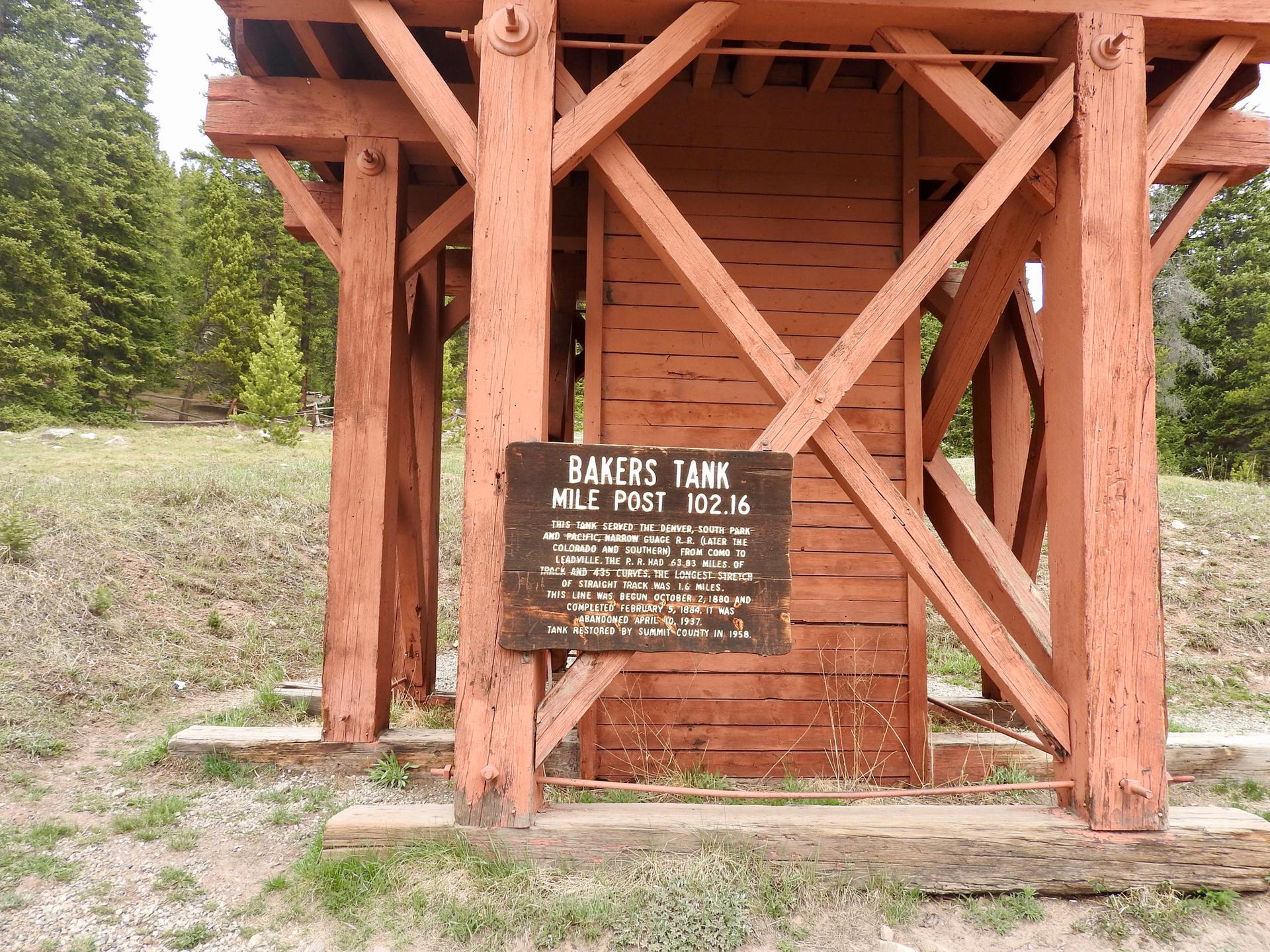 Wooden structure with a sign in a grassy area, surrounded by trees.