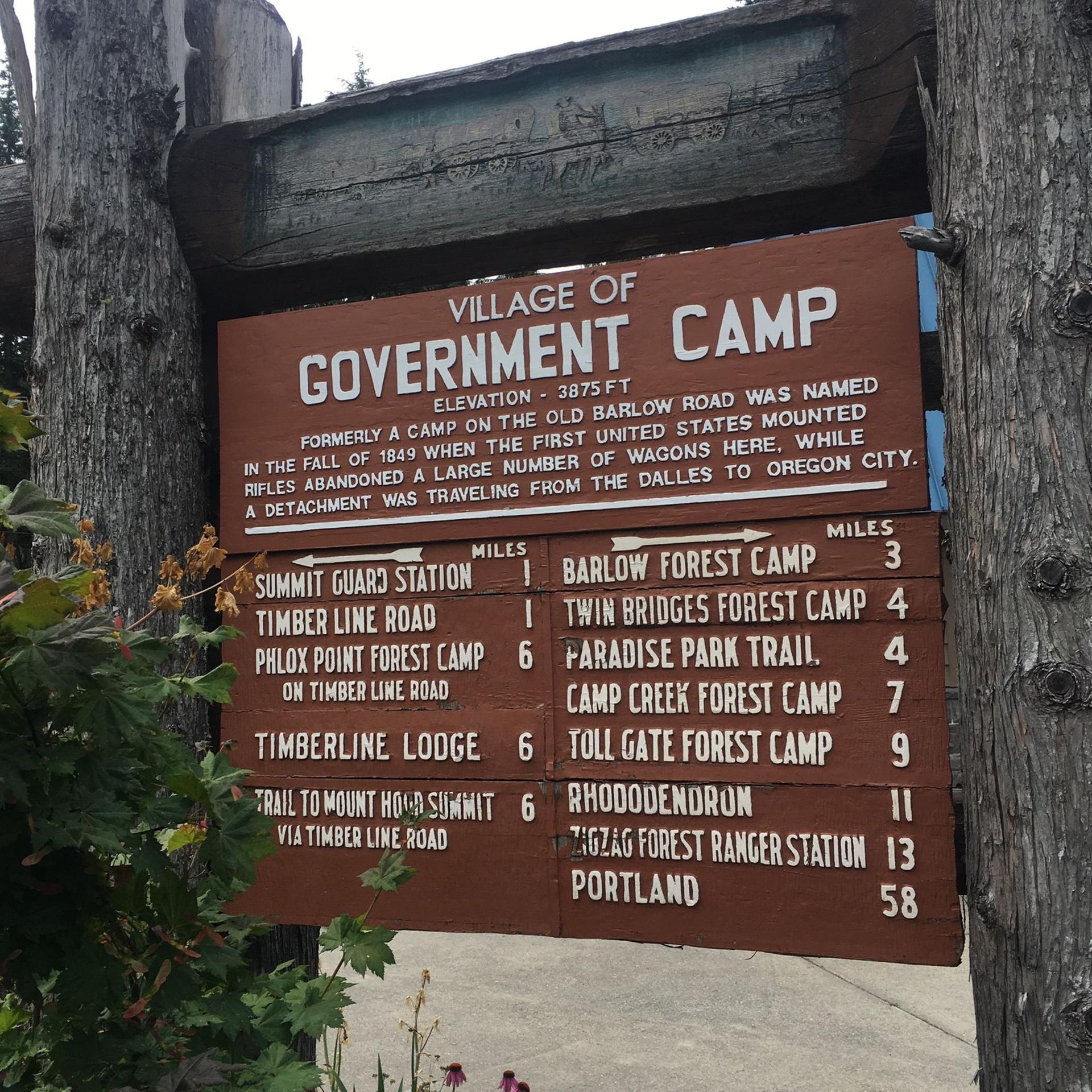 A rustic wooden sign with text and mileage information, attached to a tree.