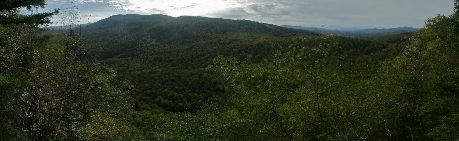 Panoramic view of lush green forested mountains and valleys under a cloudy sky.