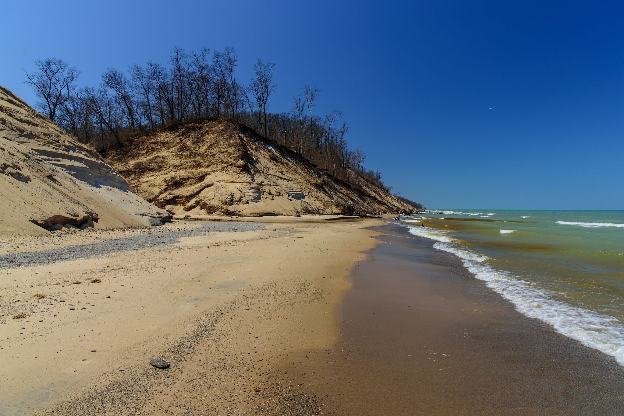Sandy beach with waves, steep sandy cliffs, and a clear blue sky. - Dunes Long Trail Alternates