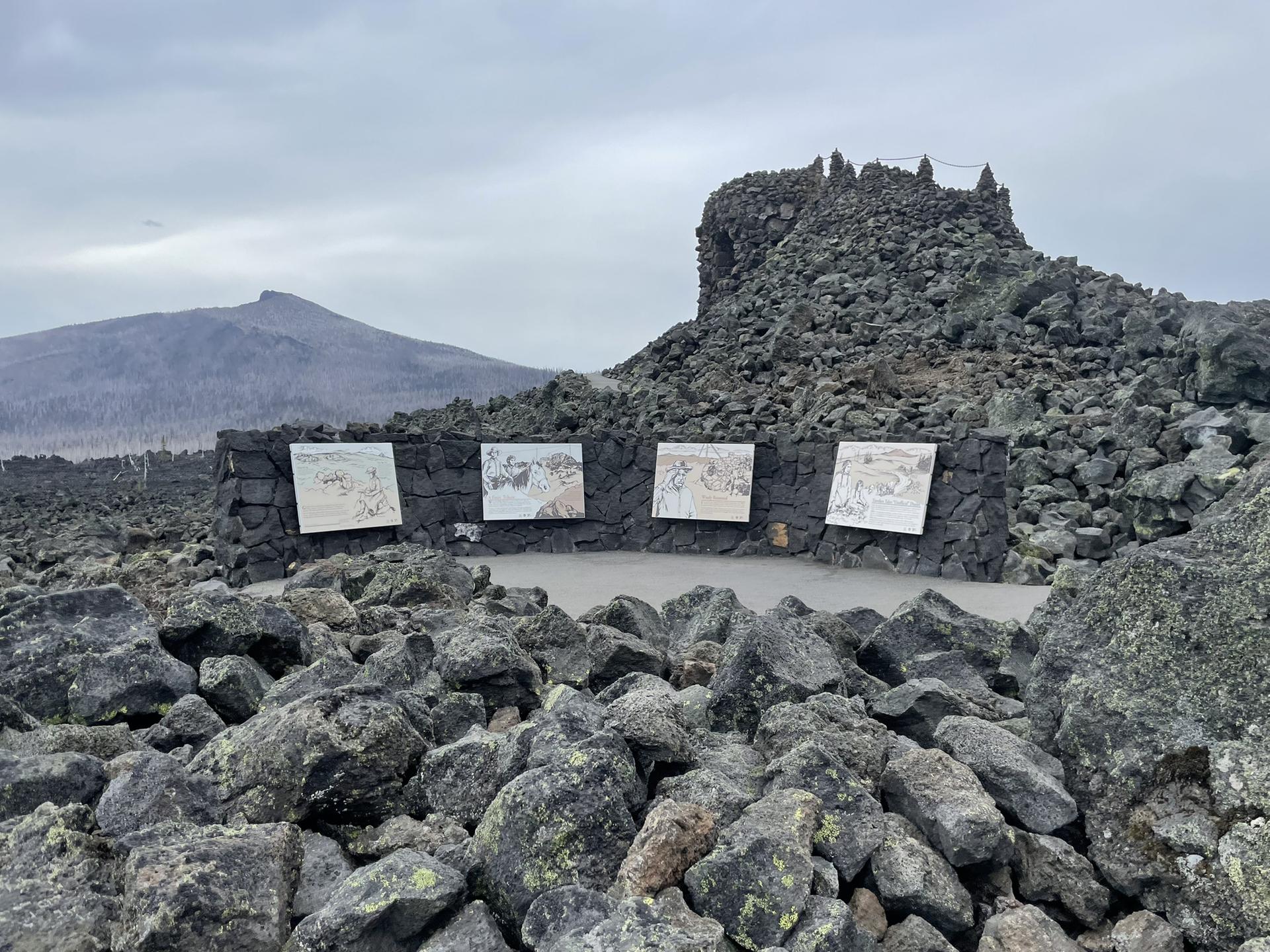 Information panels on a stone wall amidst rocky terrain under an overcast sky.