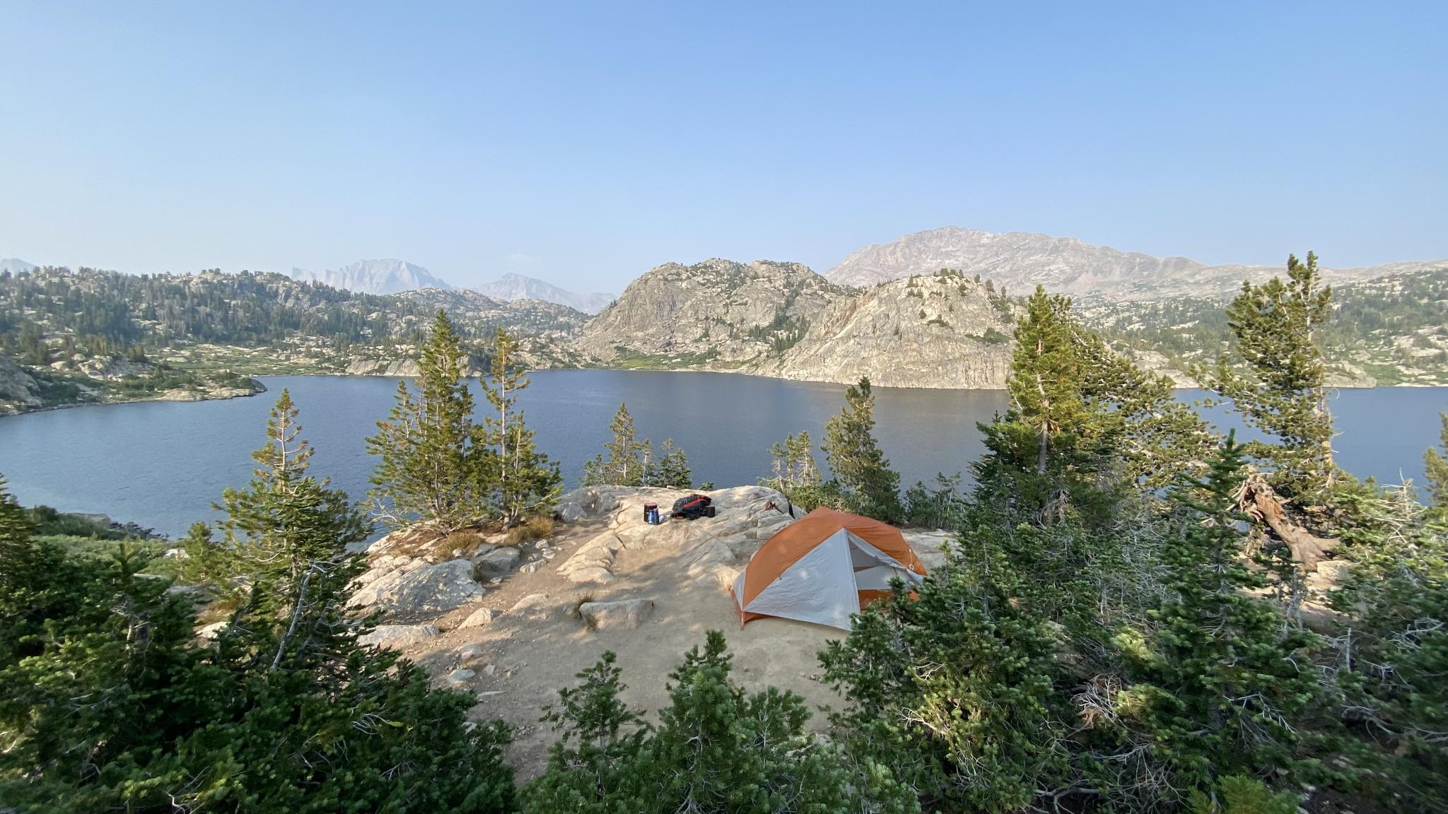 Orange tent on a rocky outcrop overlooking a large lake and mountains.