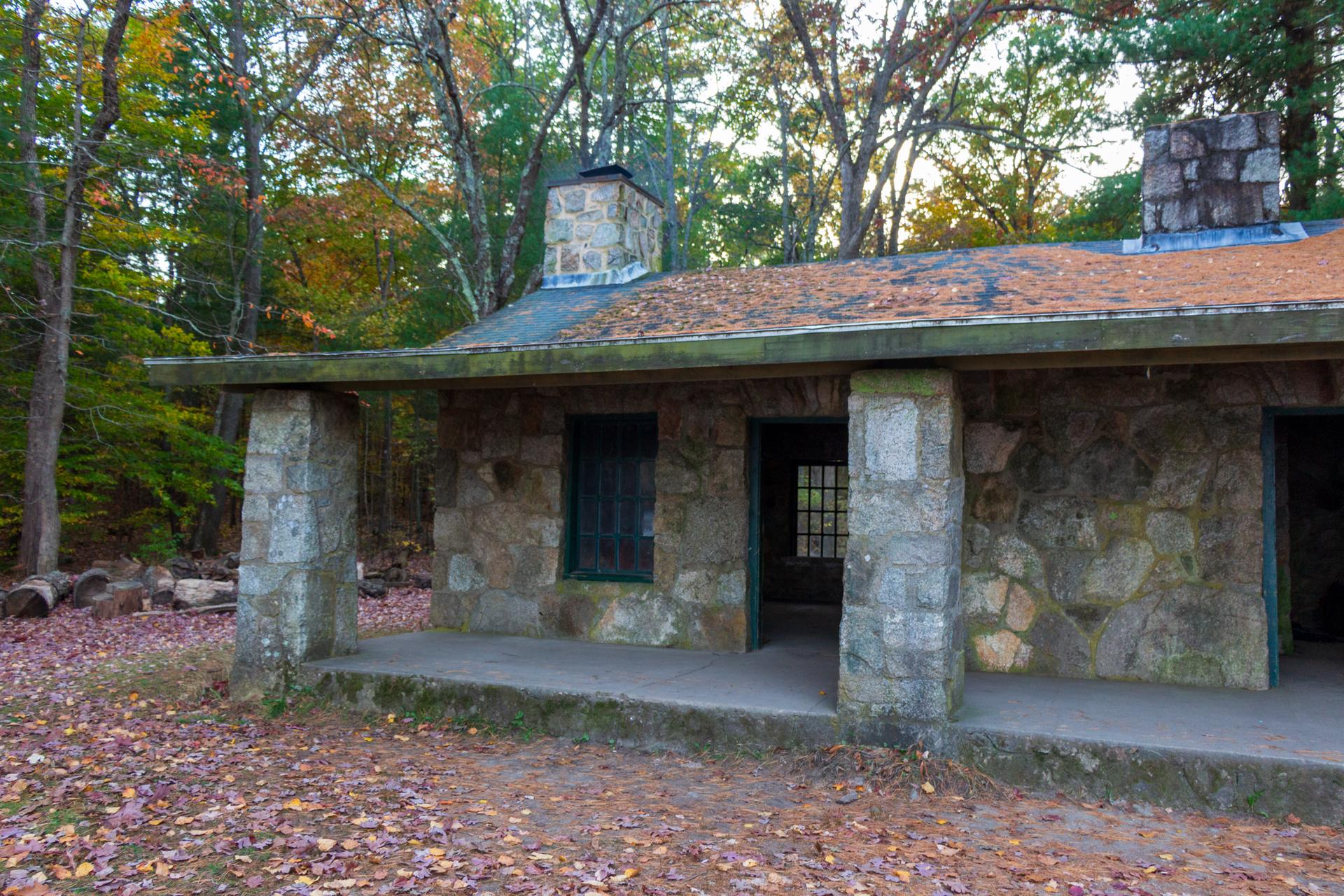 Stone building with a porch and two chimneys, surrounded by autumn leaves.