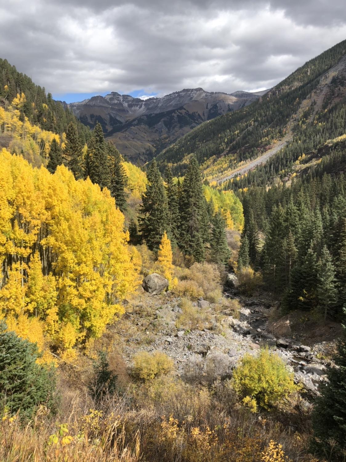 Overcast view of a steep mountain valley with a river and golden trees.