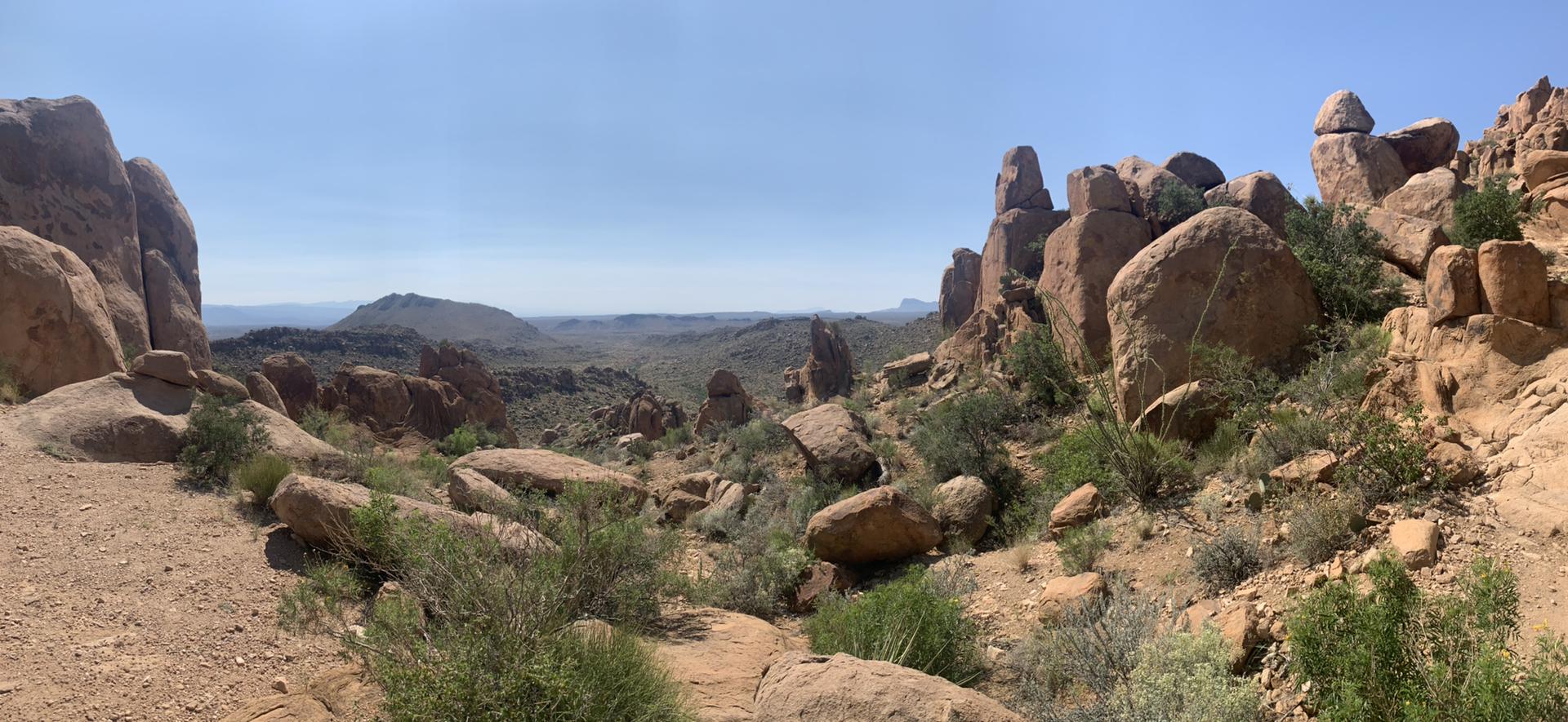 Panoramic view of a rocky desert landscape with distant mountains under clear sky.