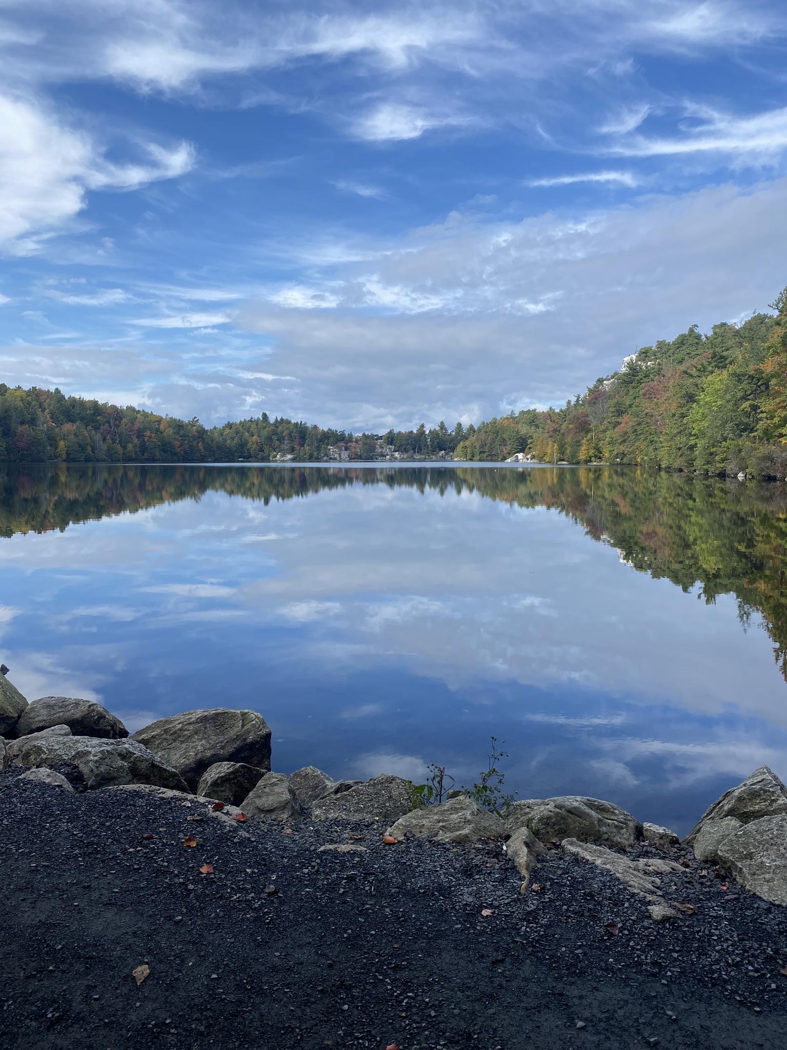 A calm lake reflects blue sky and autumn trees under a bright sky.