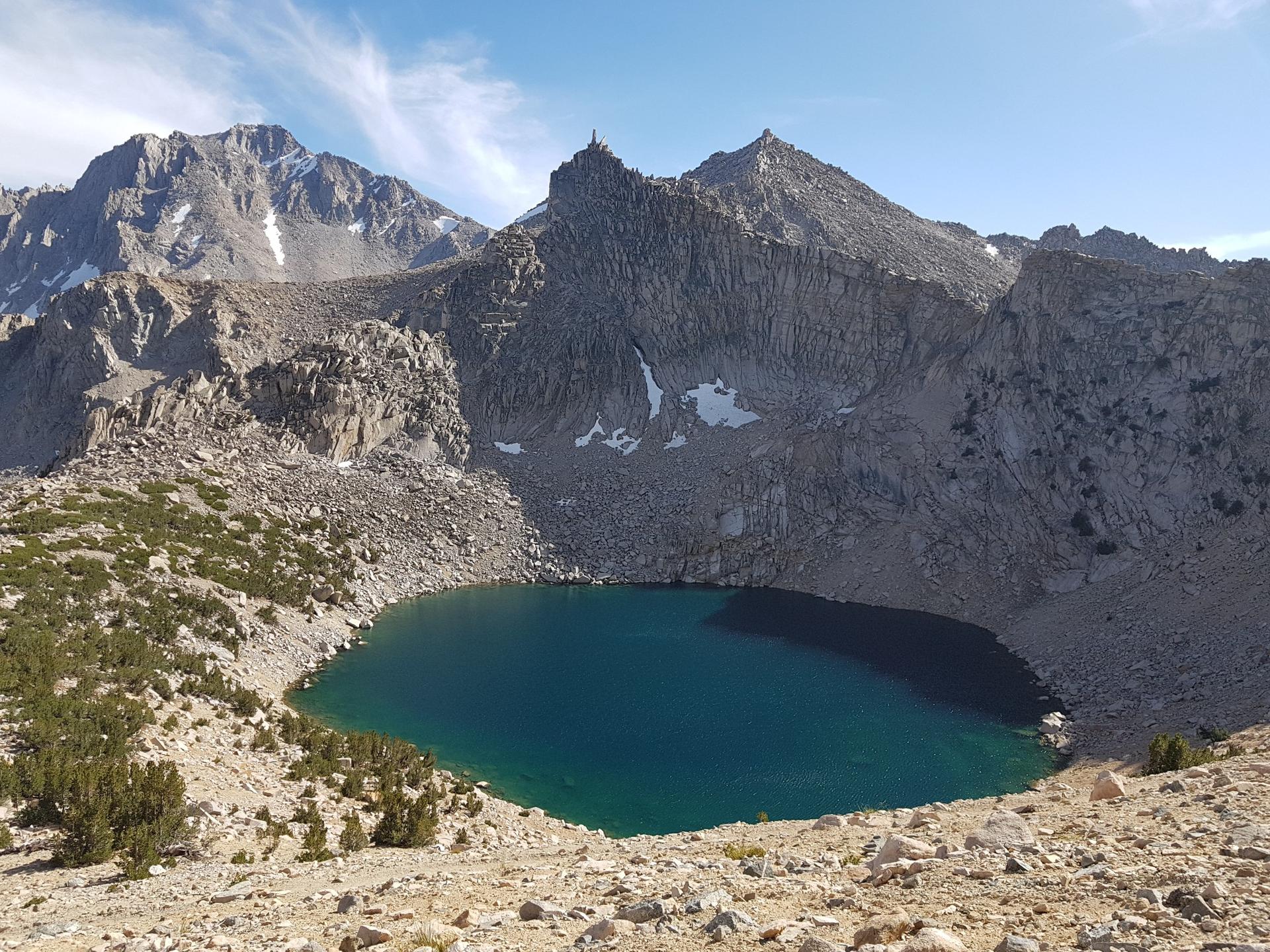 A deep blue alpine lake nestled among rugged, snow-dusted mountains on a sunny day.