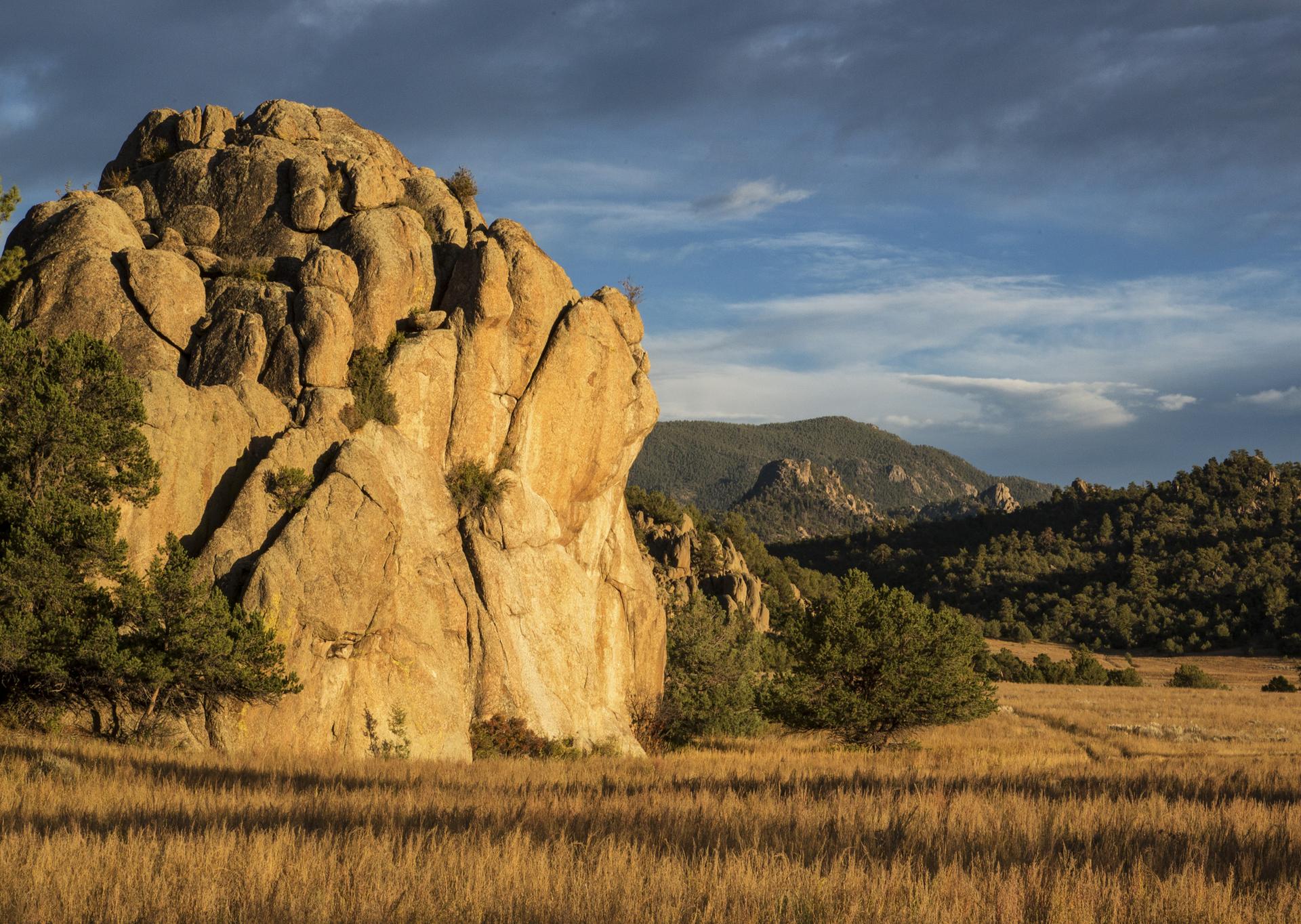Golden hour light illuminates a large rock formation and a dry grassy field.
