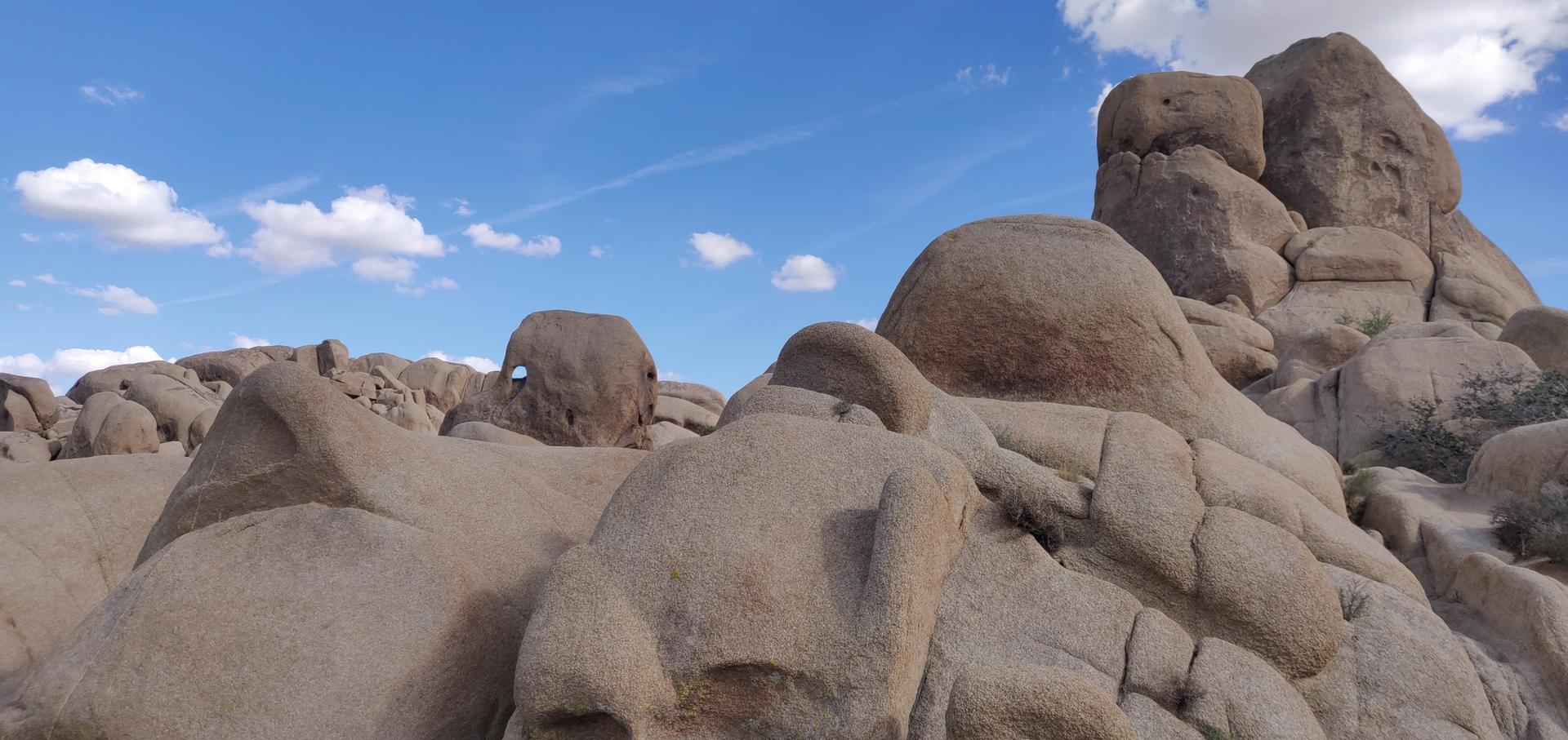 Rounded rock formations dominate a desert landscape under a blue sky with wispy clouds.