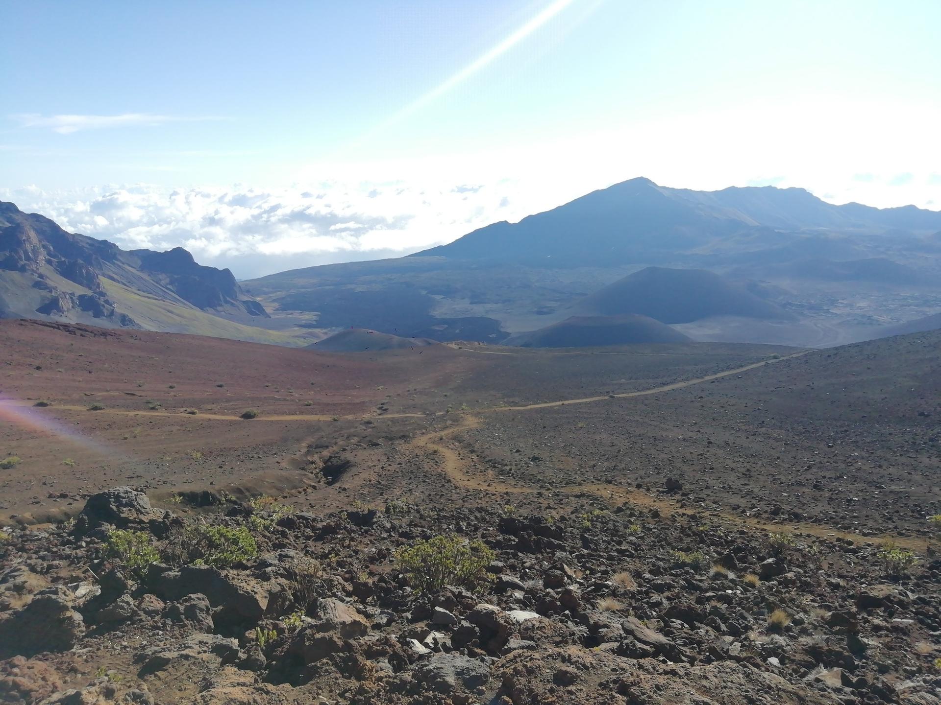 Sunny, rocky, barren landscape with a distant mountain and winding dirt path.