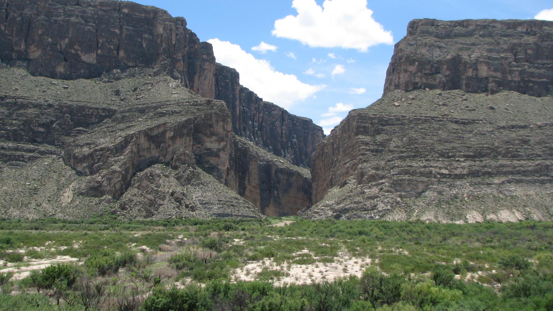 A deep rocky canyon with steep walls under a bright blue sky.