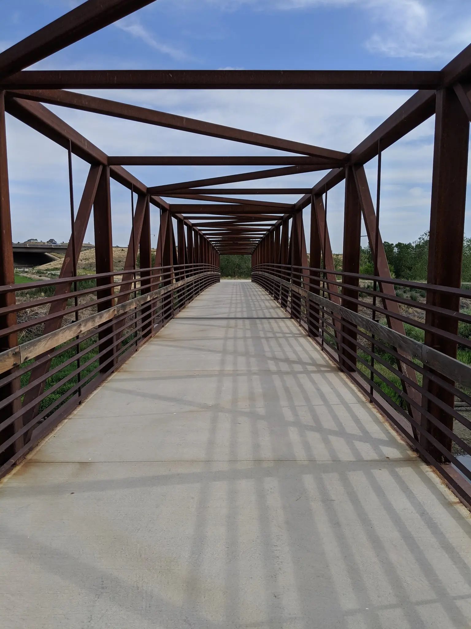 Long, rusty metal truss bridge with a concrete path under bright daylight. - South Platte River Bridge – South Platte River Bridge loop from Commerce City
