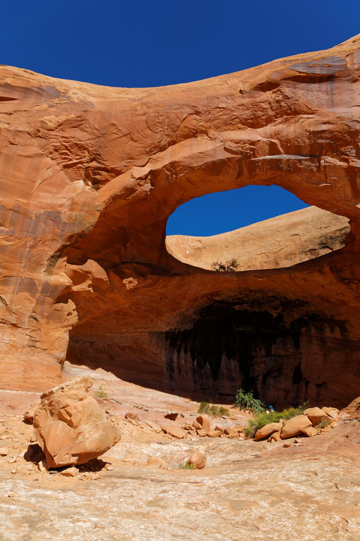 A large natural rock arch frames the bright blue sky in a desert.