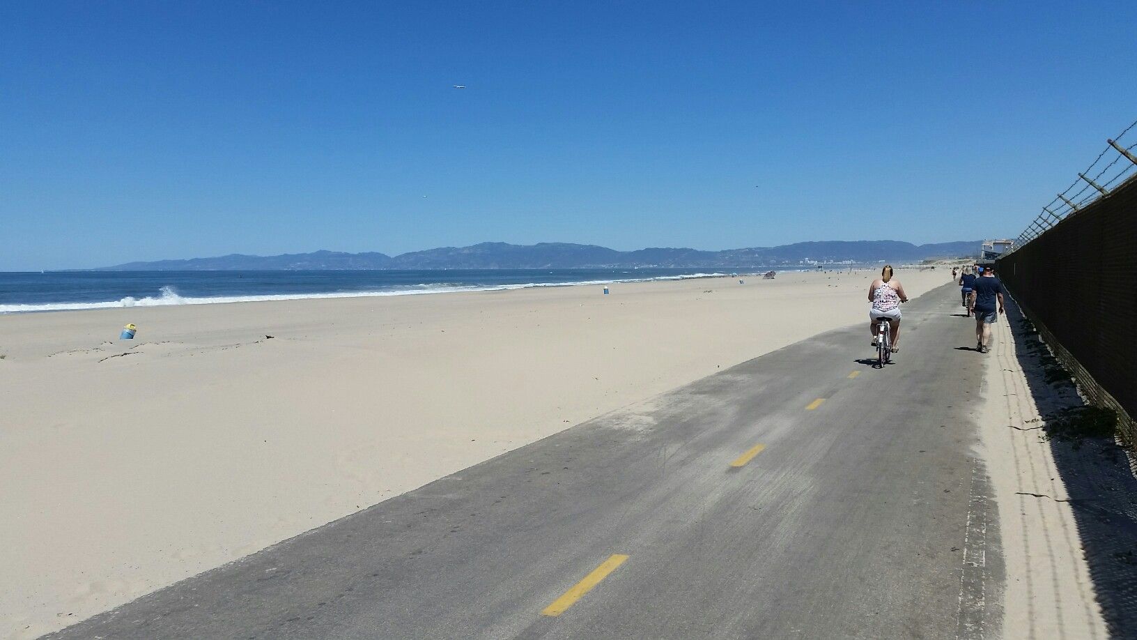 Sunny beach with people cycling on a paved path beside the ocean. - Palos Verdes Classic Donut Loop
