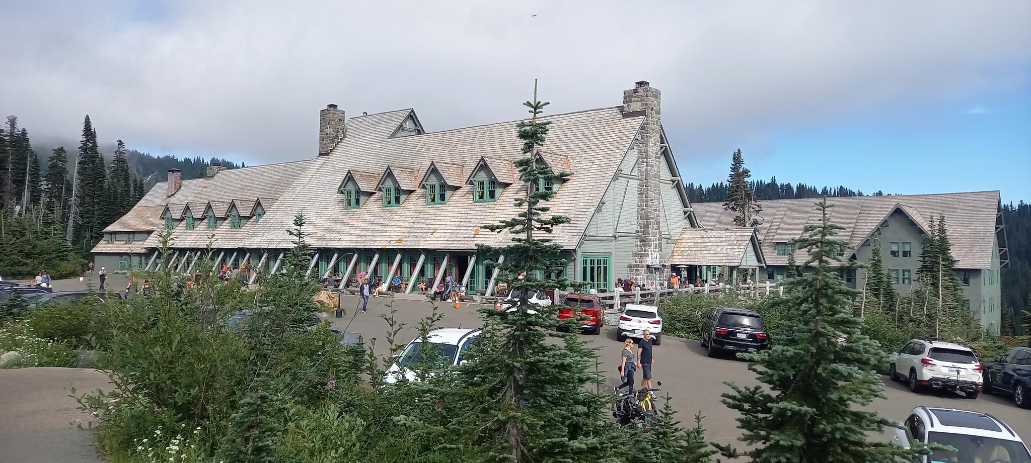 Large rustic lodge building with people and cars in a parking lot.
