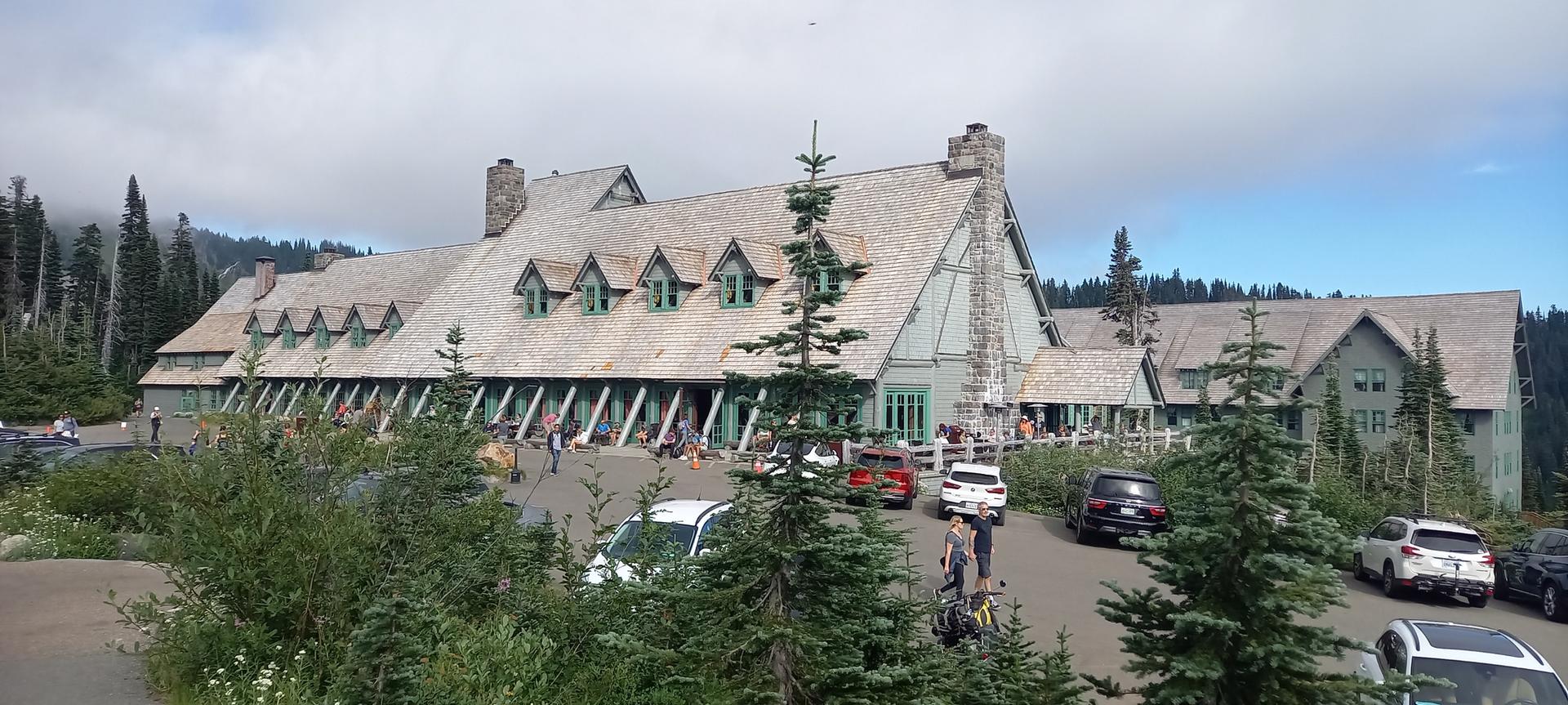 Large rustic lodge building with people and cars in a parking lot.