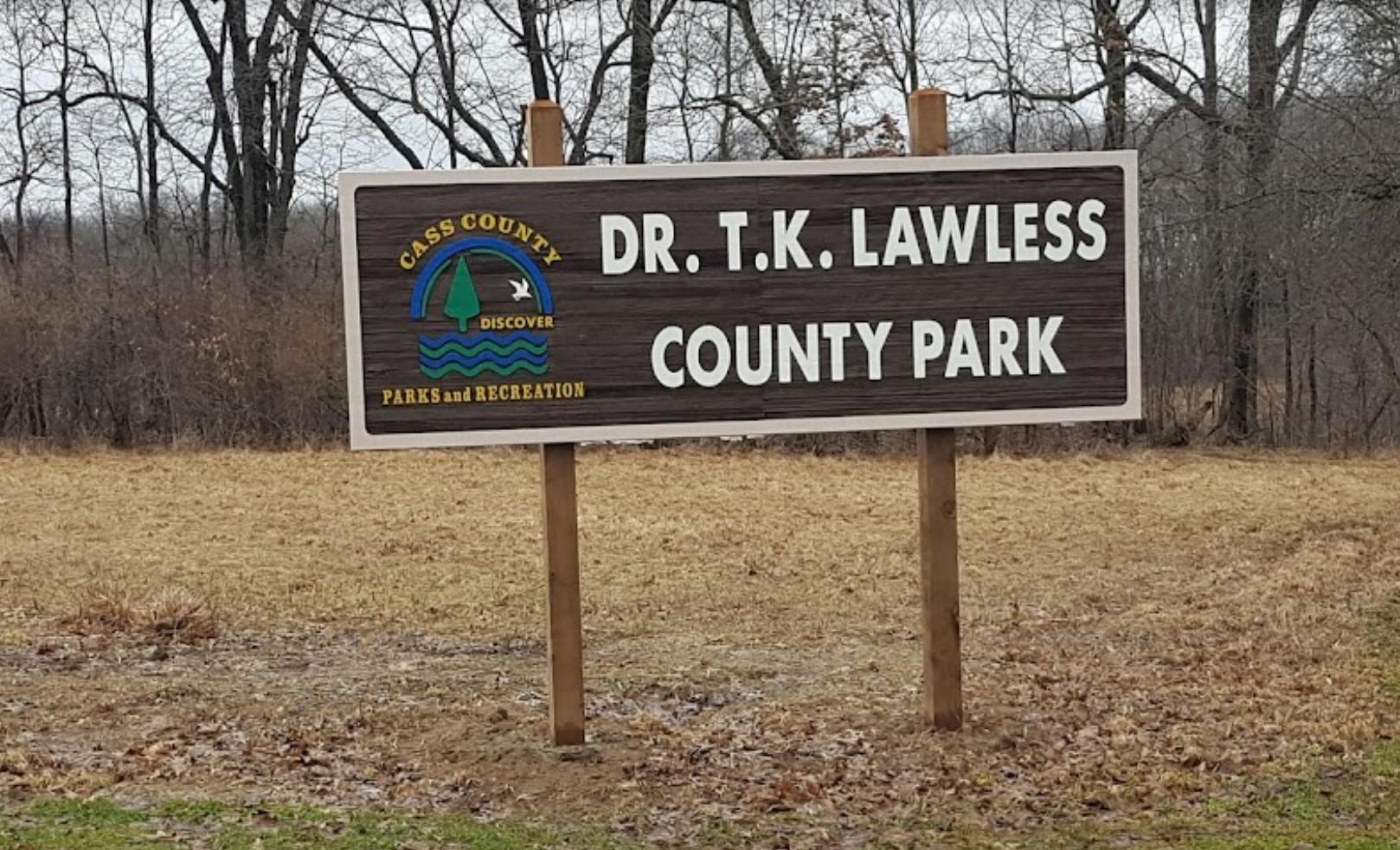 A brown and white park sign stands in dry grass with bare trees.
