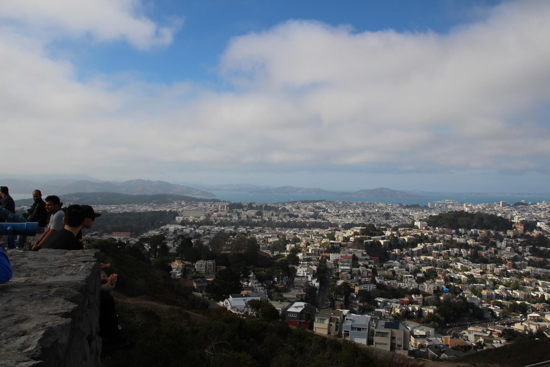 People observing a vast city panorama from a viewpoint under cloudy sky.