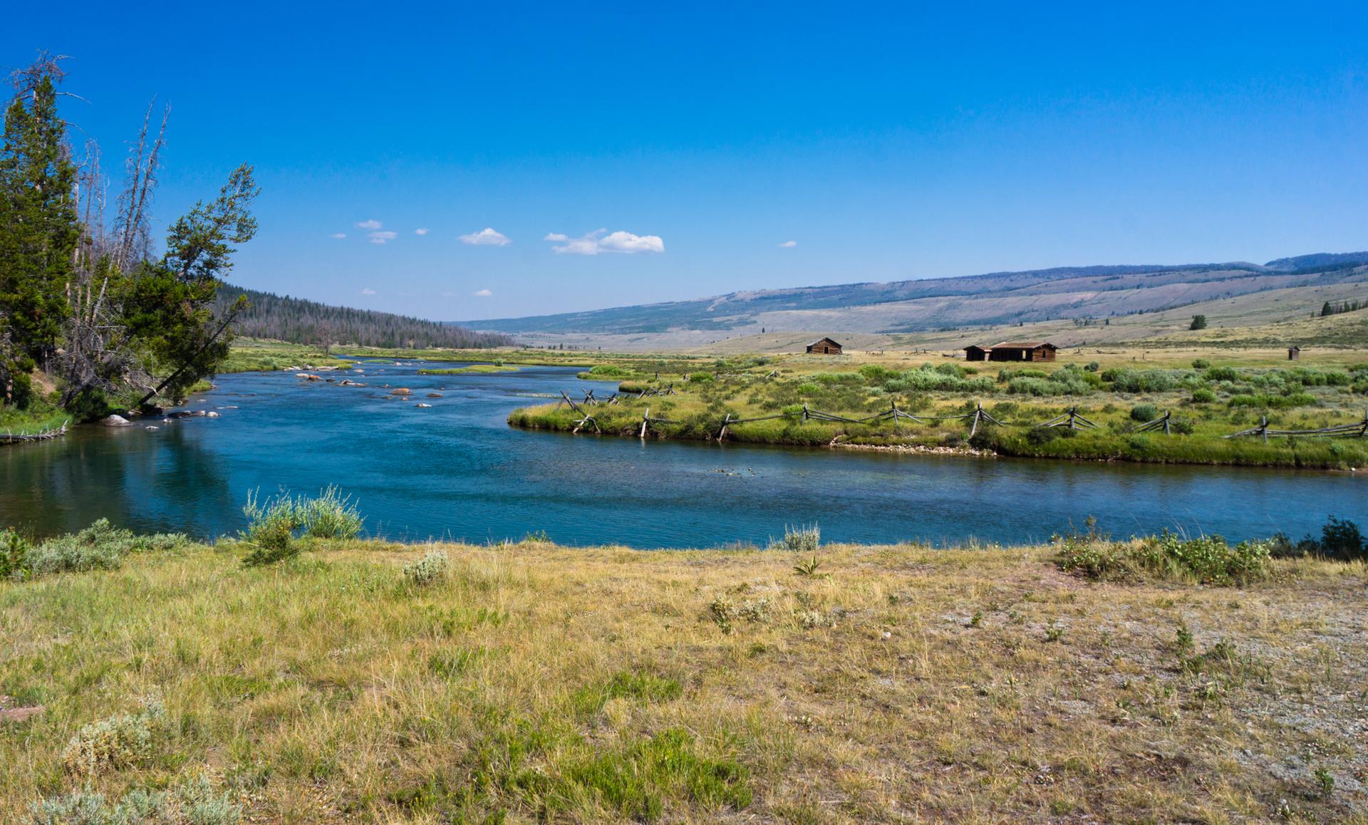 Wide blue river winding through grassy plains with distant cabins.