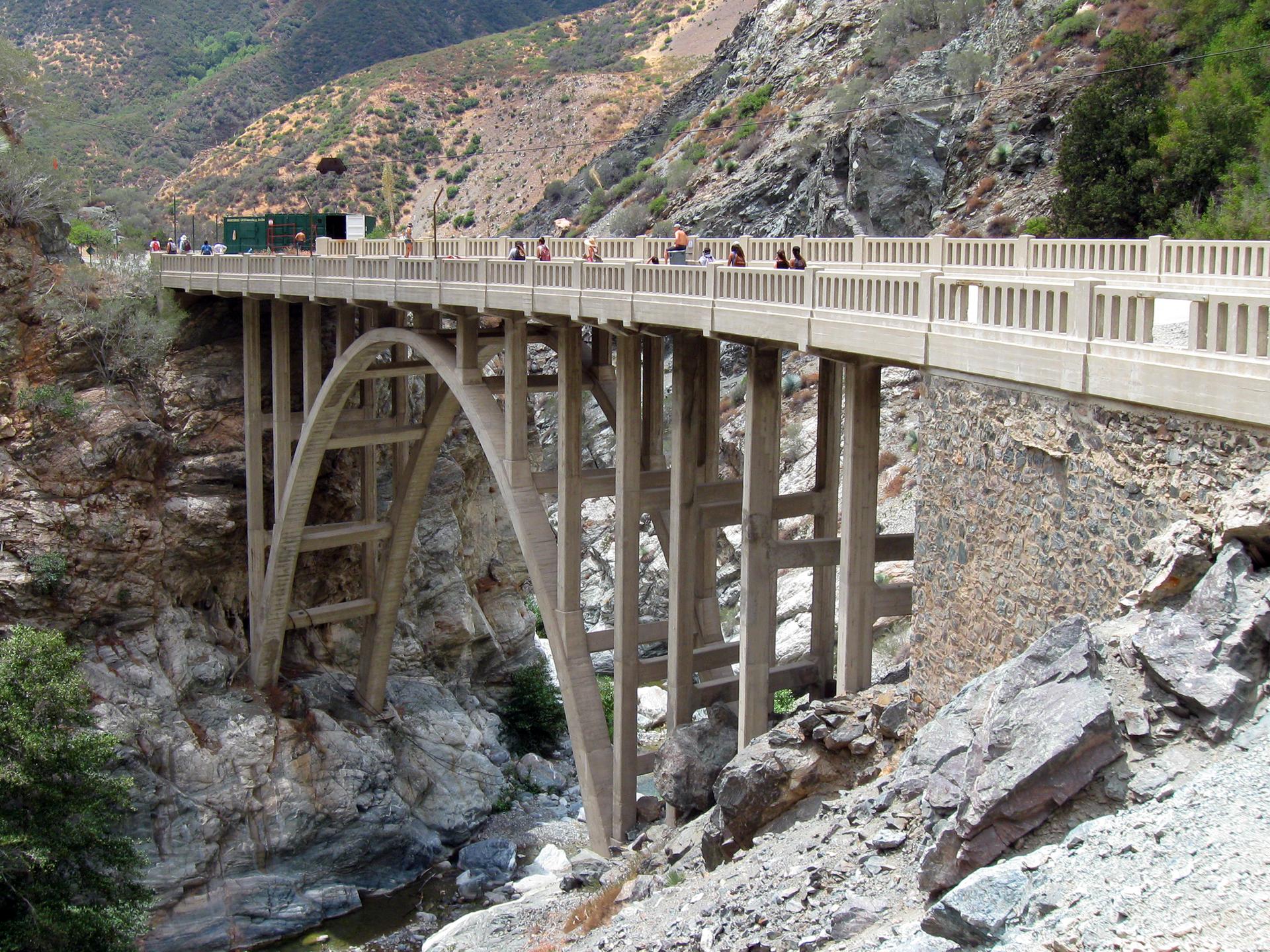People stand on a large concrete arch bridge over a rocky canyon.
