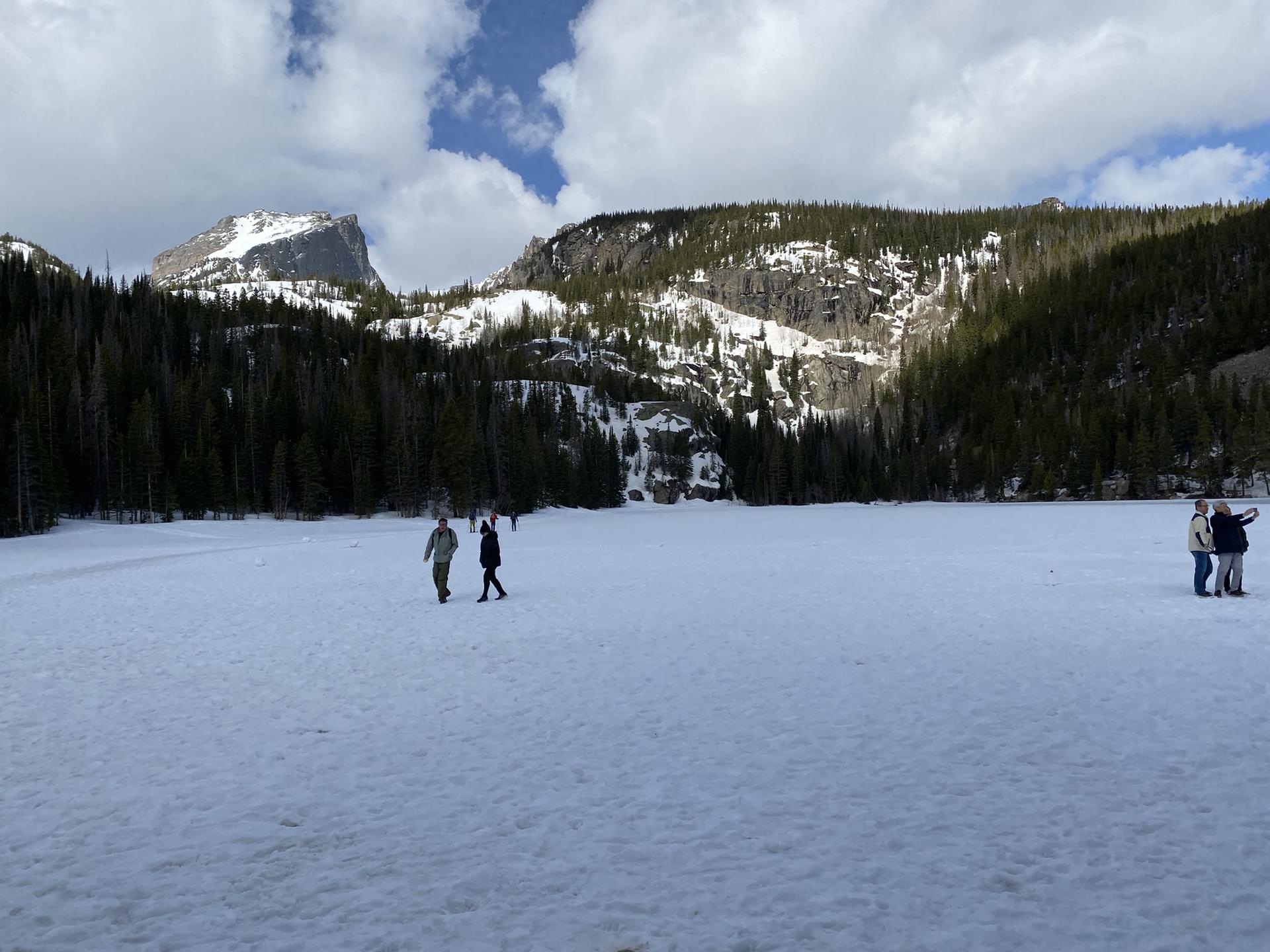 People walk across a frozen, snow-covered lake with mountains in background.
