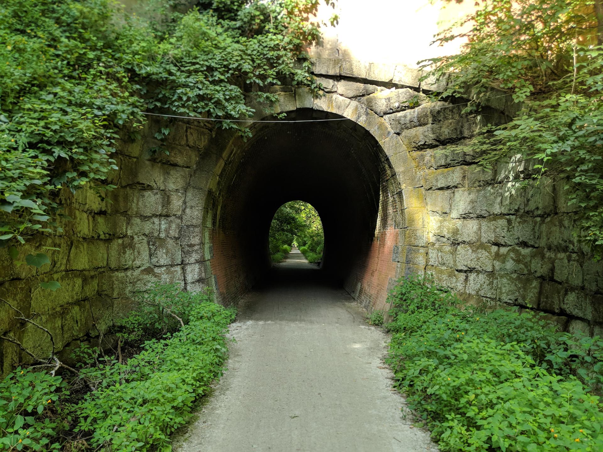 A stone tunnel with a path leading through, bright light at the end.