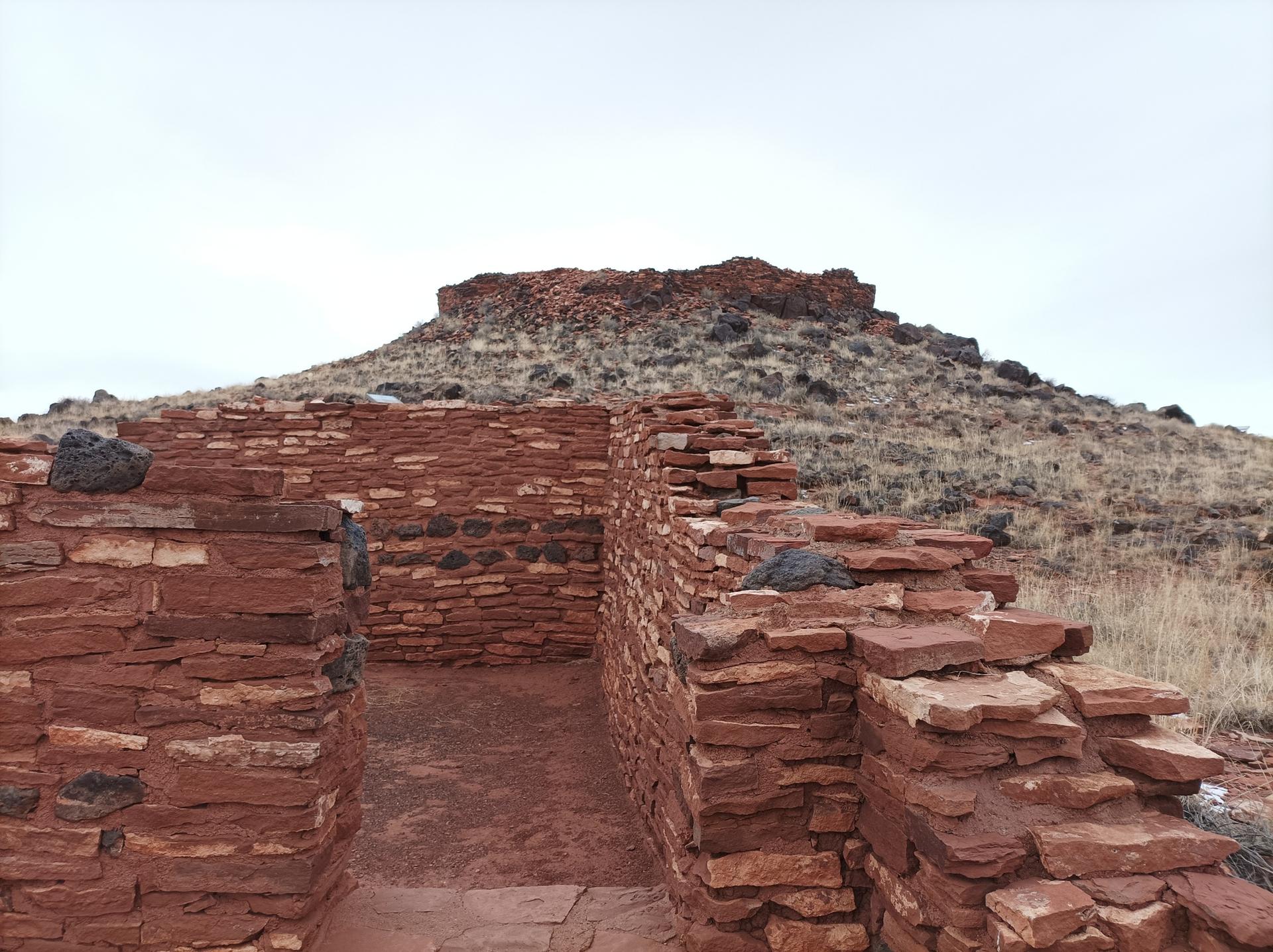 Ancient red stone ruins in the foreground, with a dry, rocky hill behind.