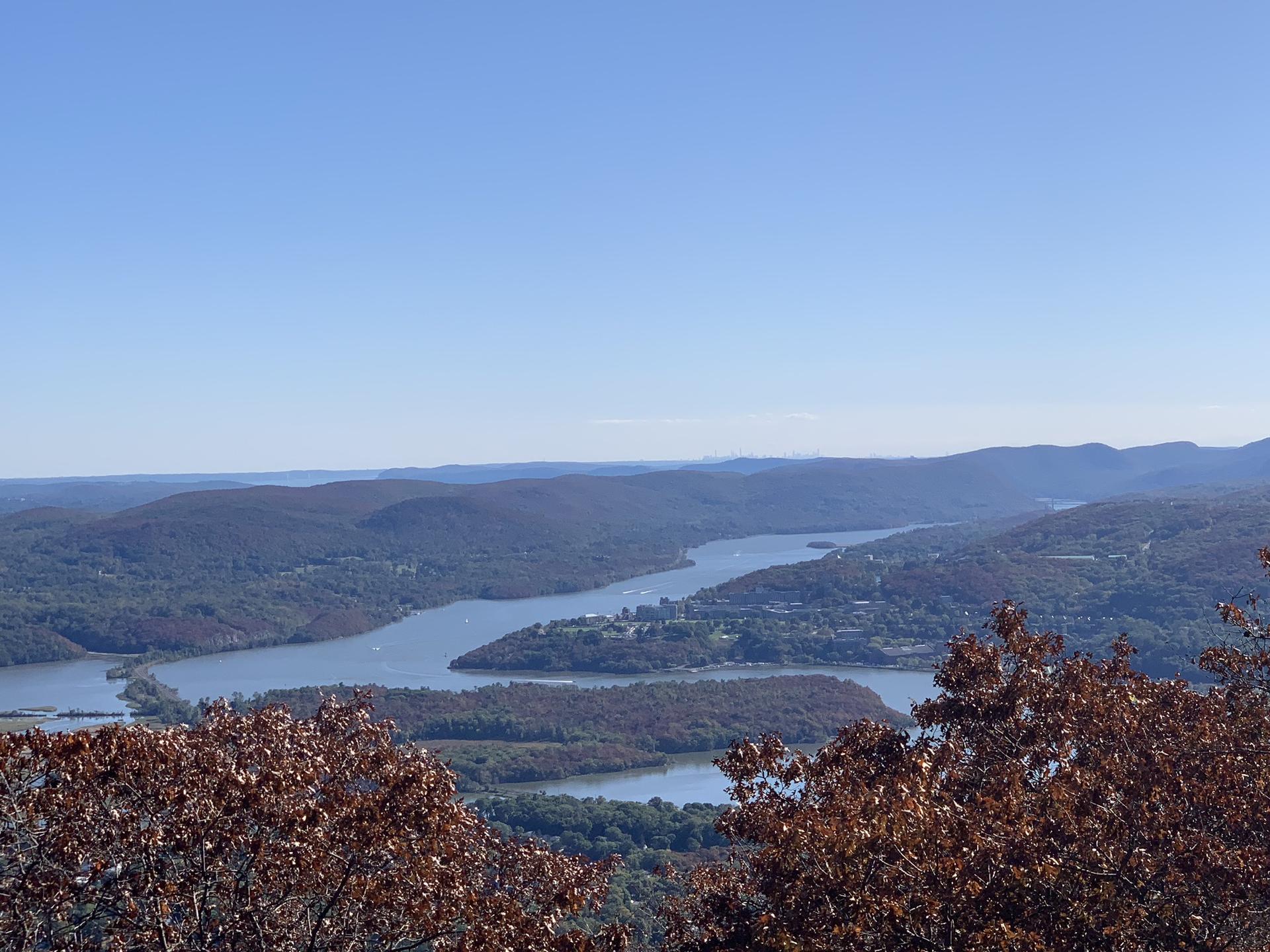 Sunny aerial view of a river flowing through forested hills under a clear sky.
