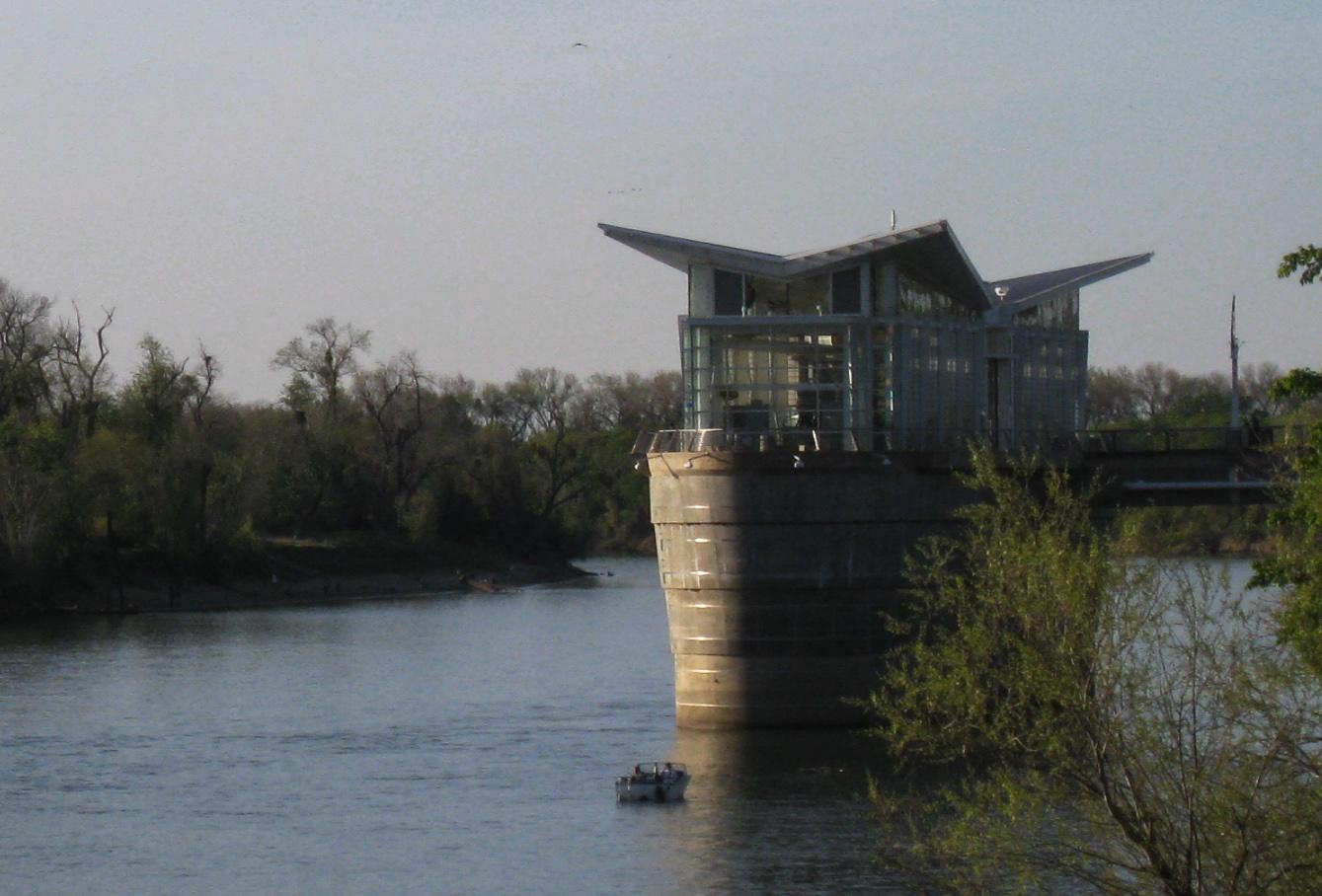 Modern building on a river with a small boat, surrounded by trees.