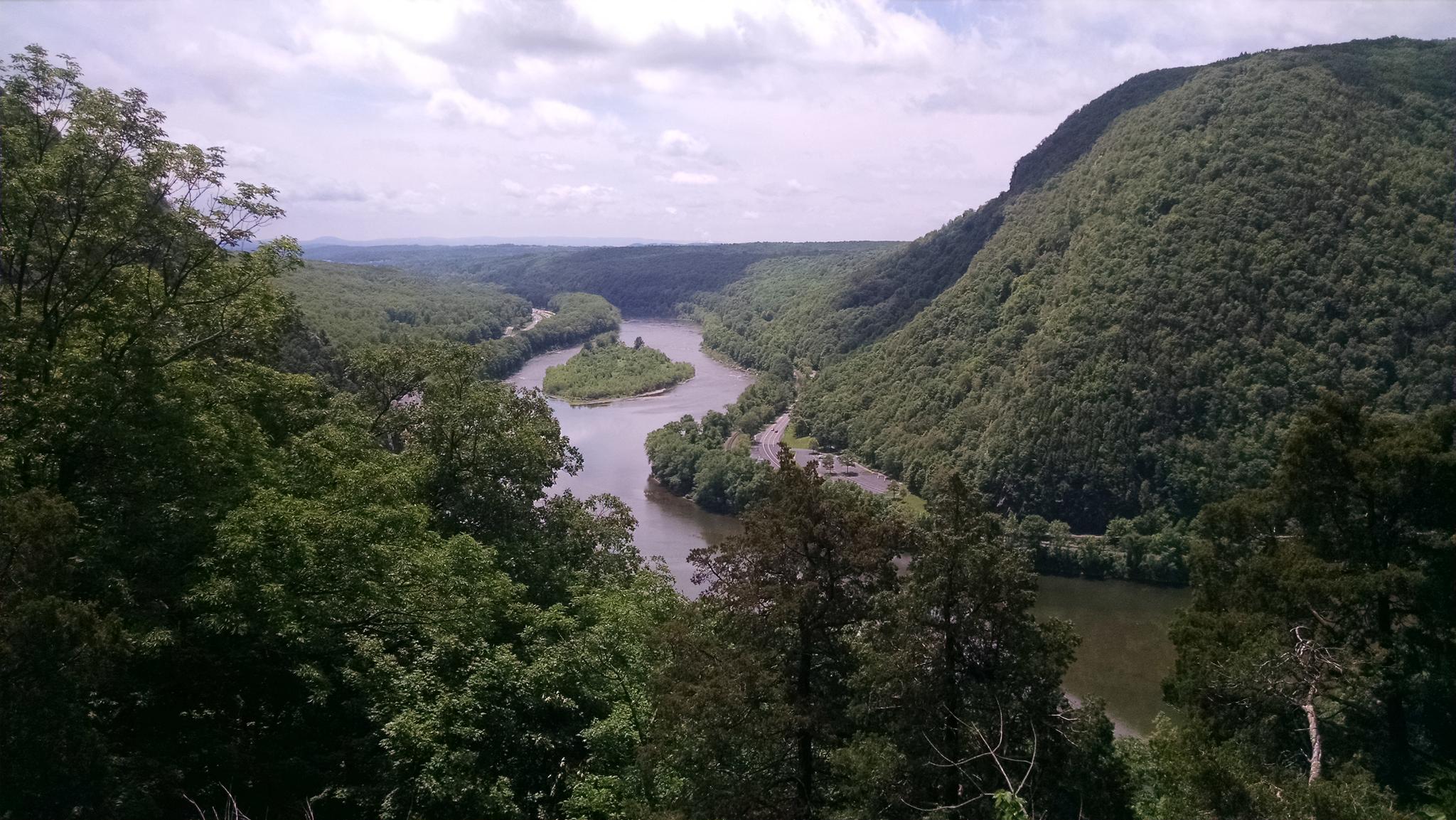 Winding river through a lush green forested valley under a cloudy sky.