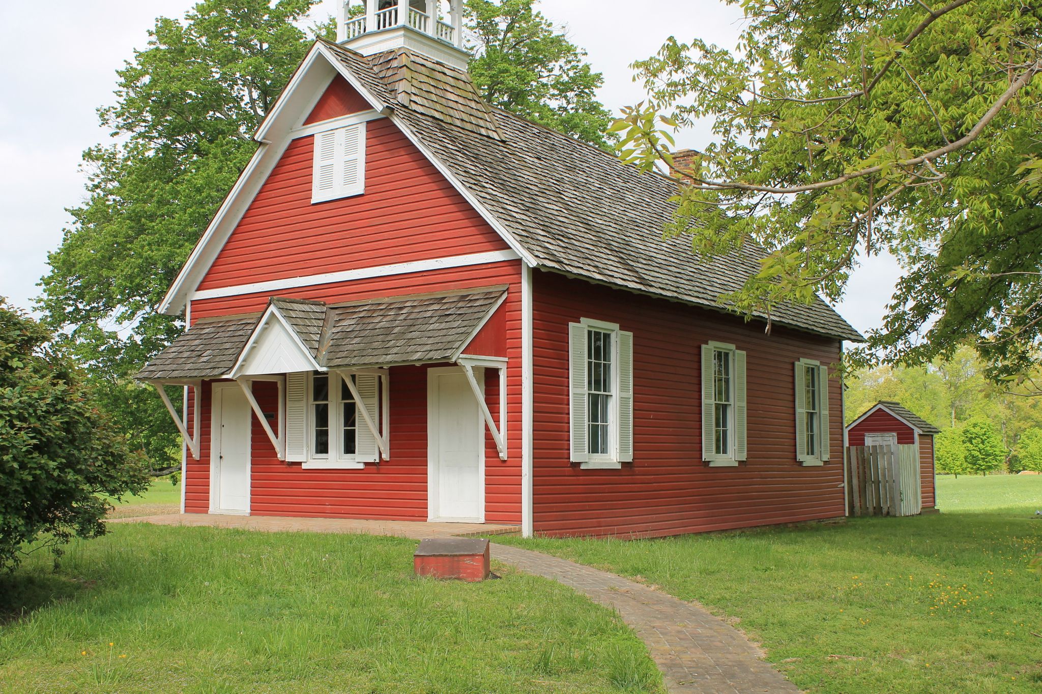 Bright red wooden building with white trim and bell tower on a grassy lawn. - Little Red Schoolhouse loop from Easton