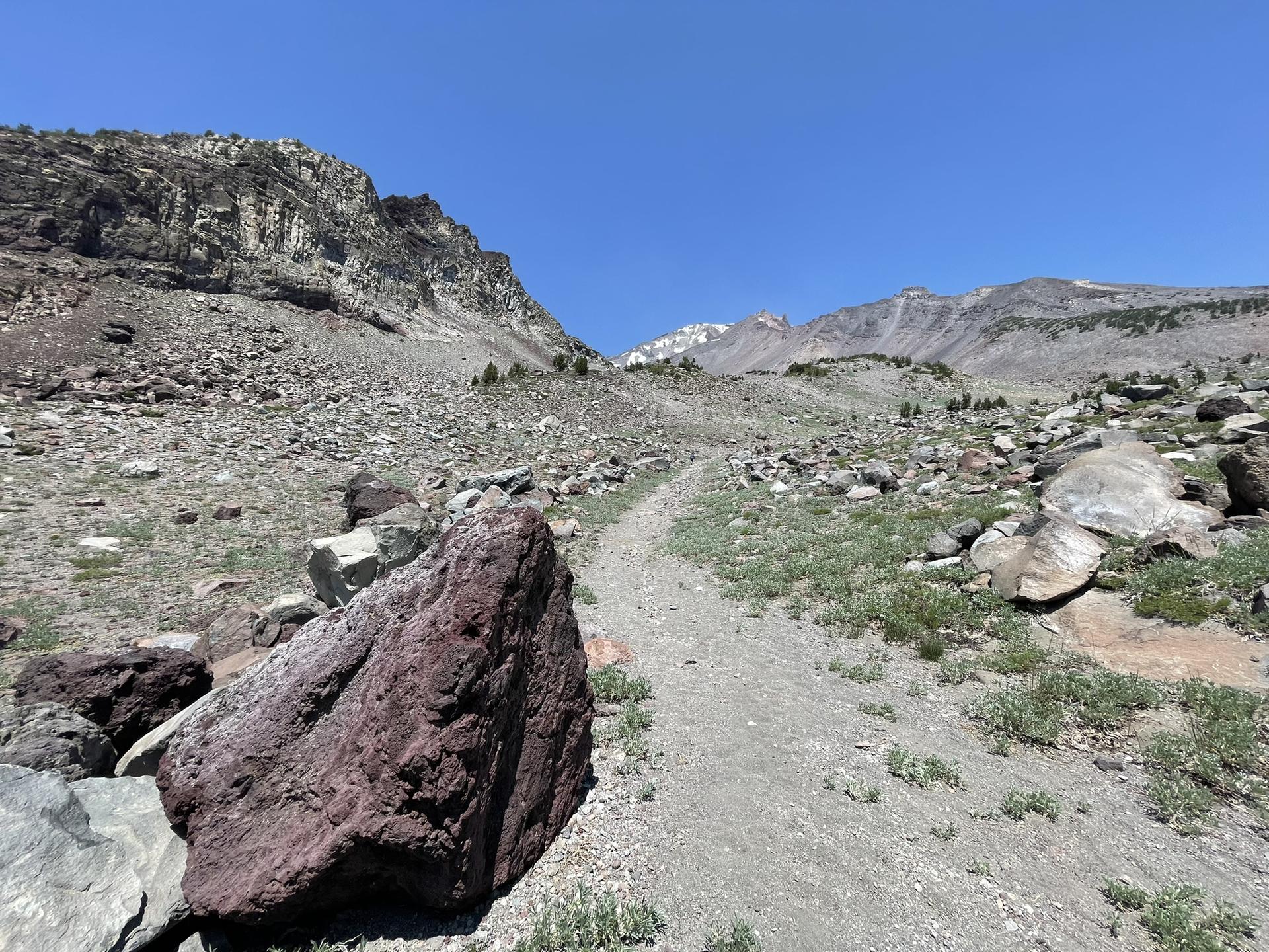 Rocky dirt trail winding through a barren mountain landscape on a clear day.