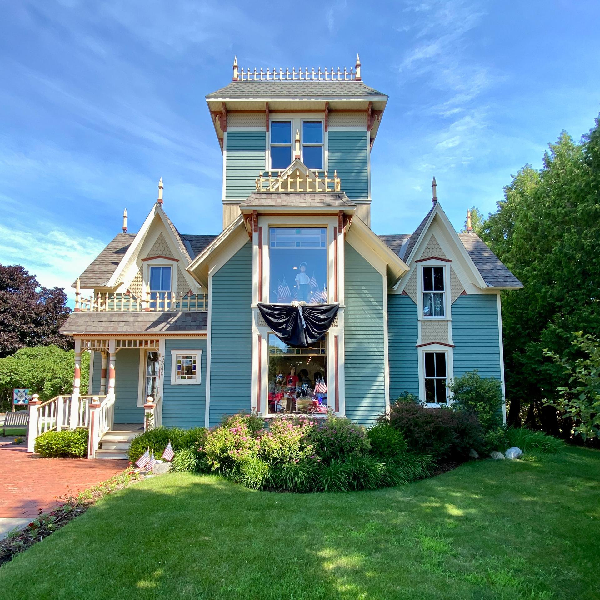 Ornate Victorian house with a green lawn under a bright blue sky.