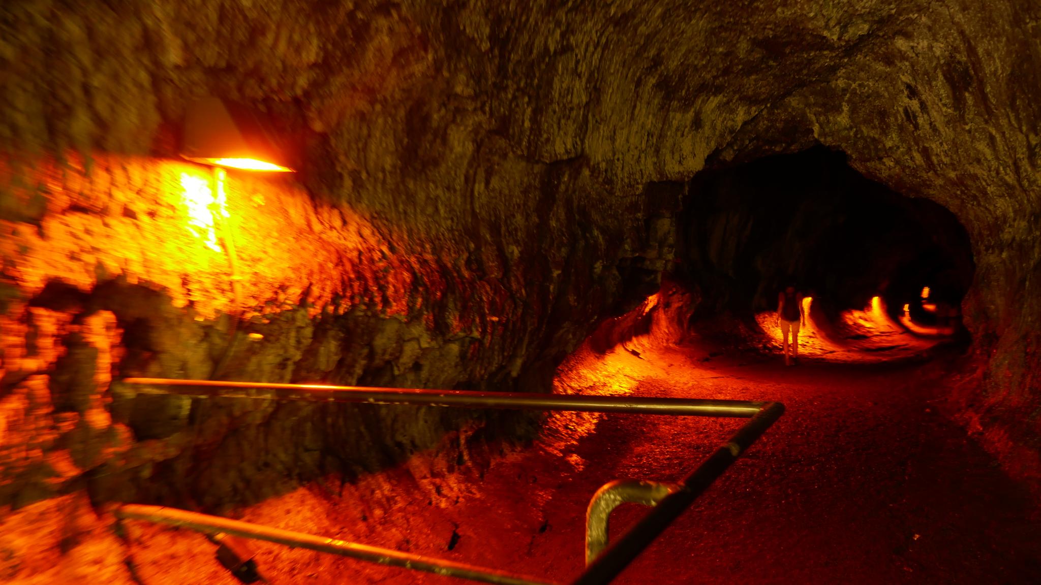 Illuminated underground lava tube with a handrail, glowing orange.