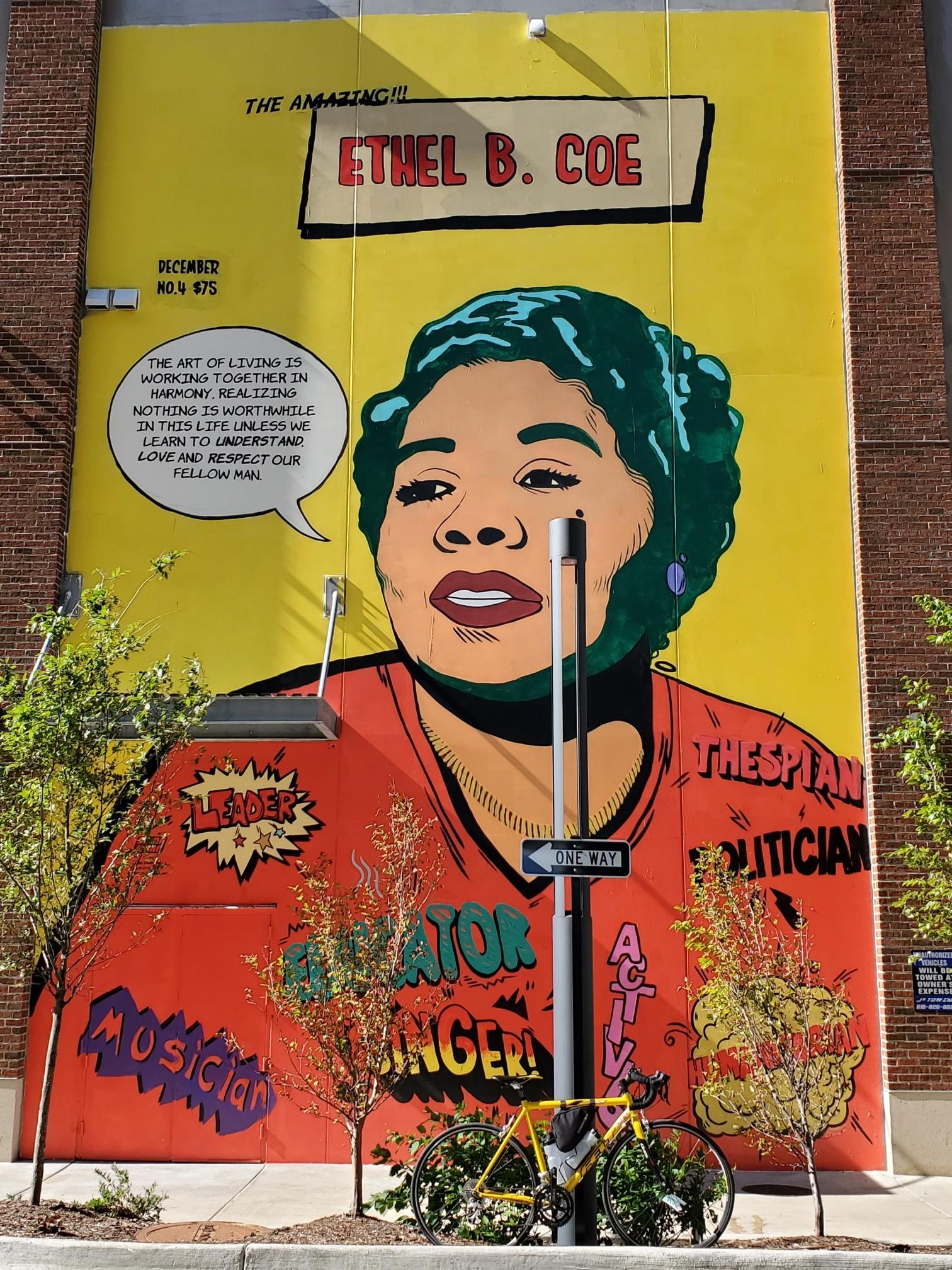 Vibrant mural of a woman's face on a yellow wall, with a bicycle below.