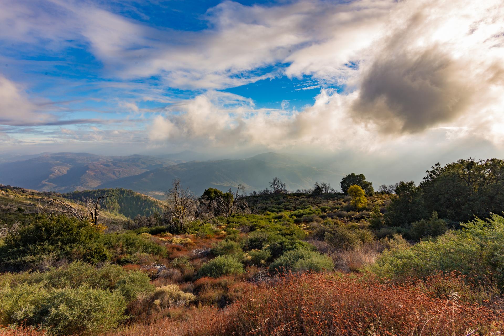 Dramatic cloudy sky over colorful hills and distant mountains at sunset.