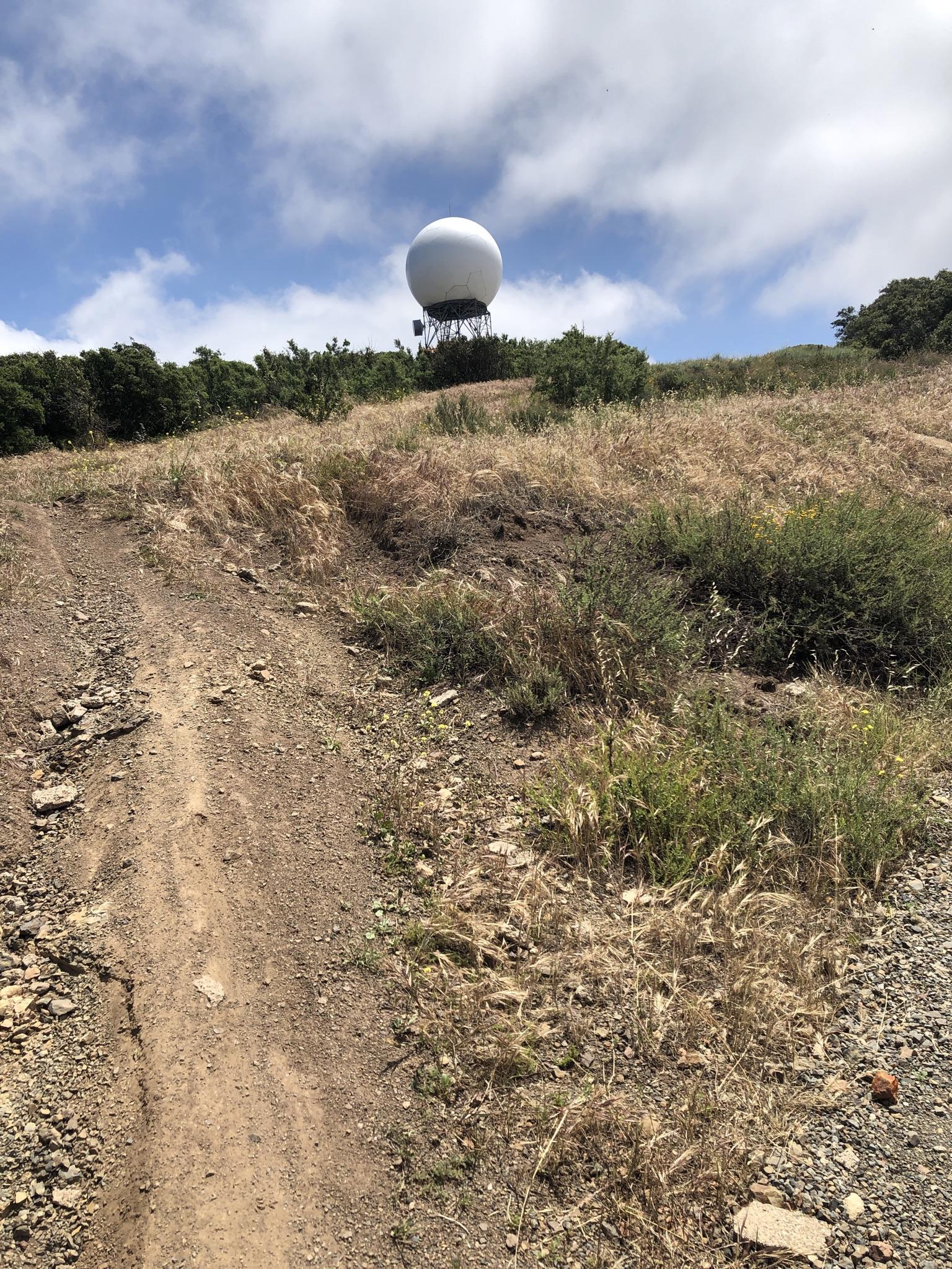 A large white spherical structure sits atop a dry, grassy hill under a cloudy sky.