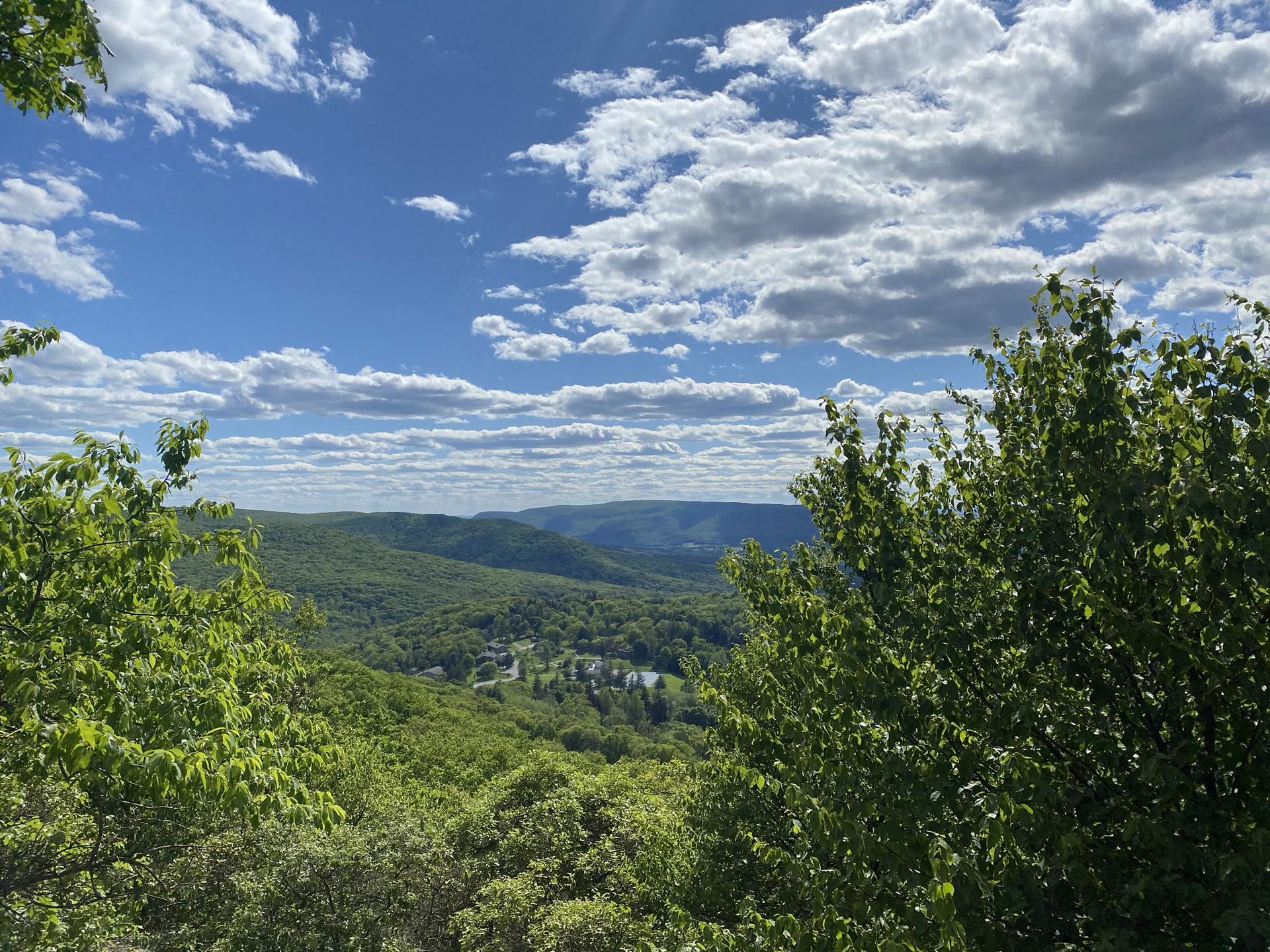 Lush green mountains and valley under a bright blue sky with white clouds.