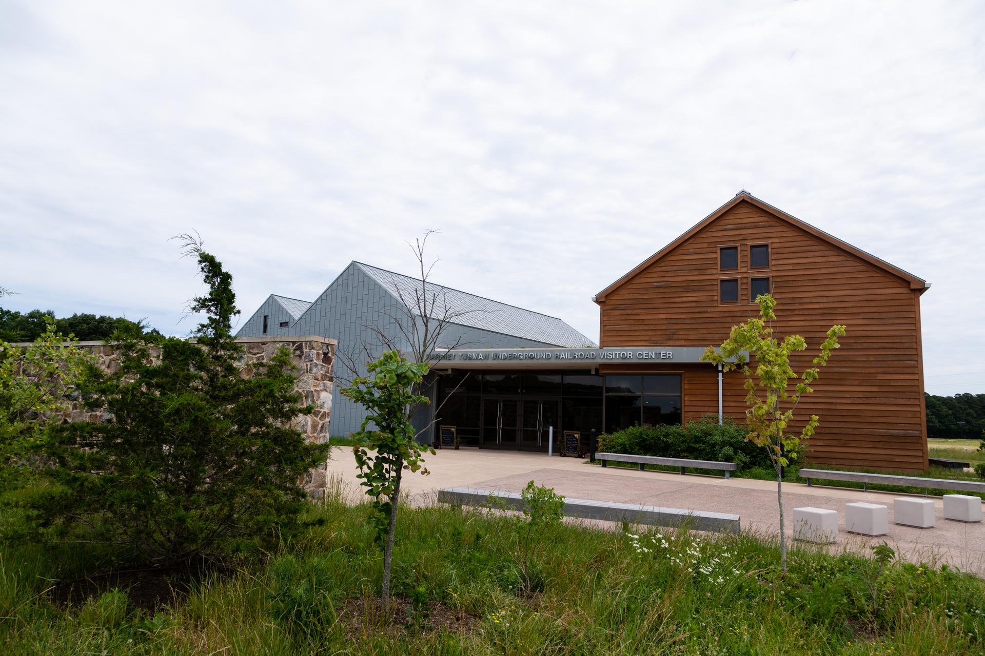 Modern buildings with wood and metal siding, paved entrance, cloudy day.