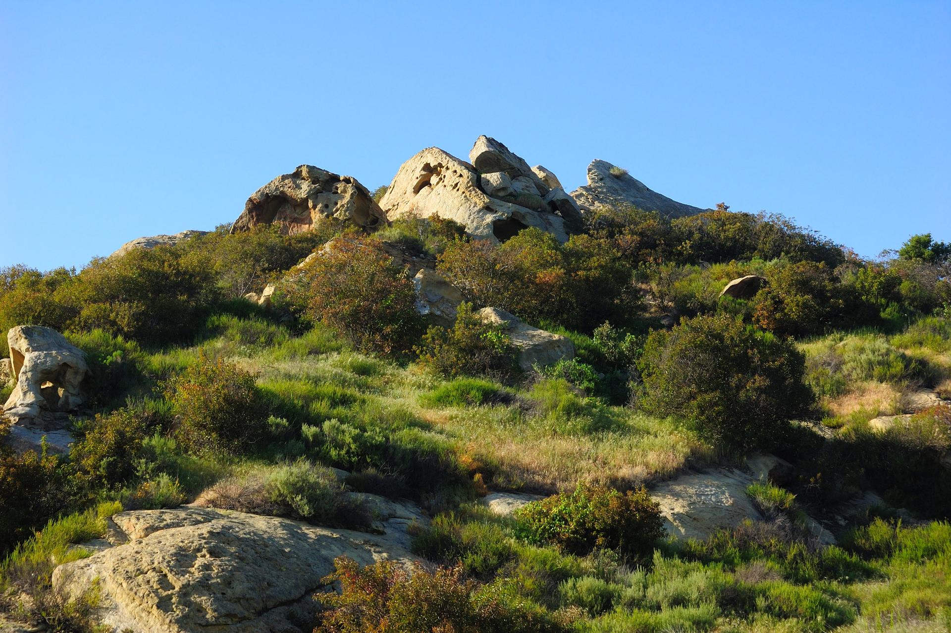 Rocky, brush-covered hillside under a clear blue sky.