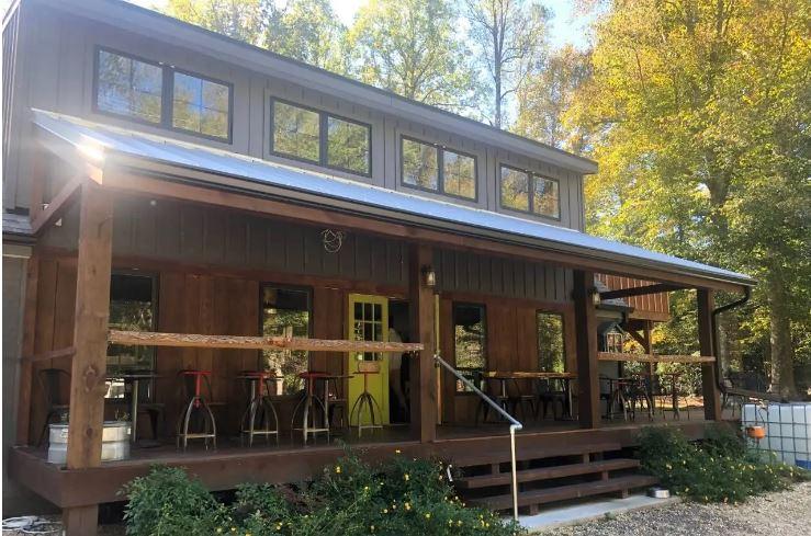 Rustic wooden building with a porch, yellow door, and outdoor seating in sunlight.