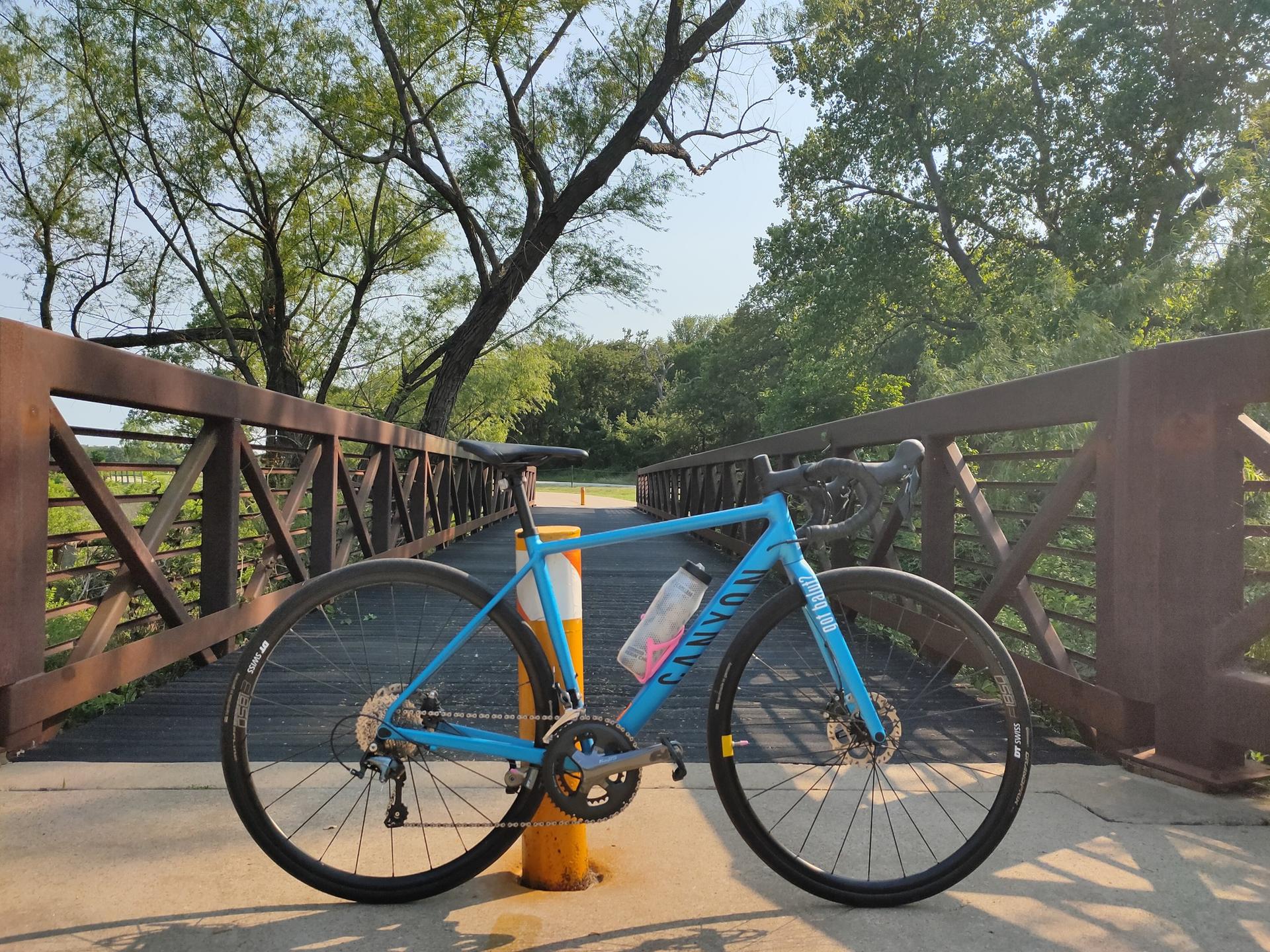 Blue road bike parked on a rustic bridge under bright, sunny skies.