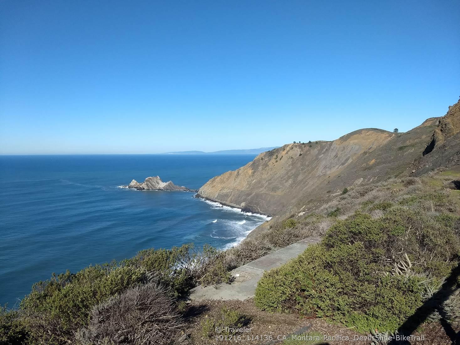 Sunny coastal landscape with ocean, sea stacks, and a winding path.