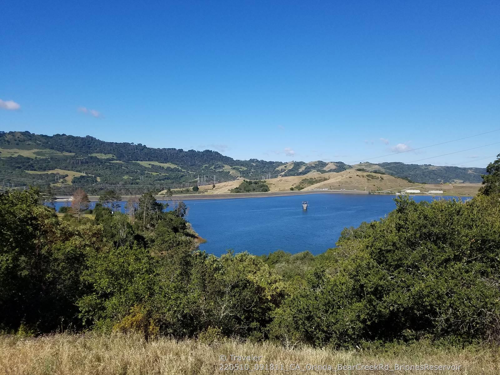 A wide blue lake surrounded by green and golden hills on a clear day.