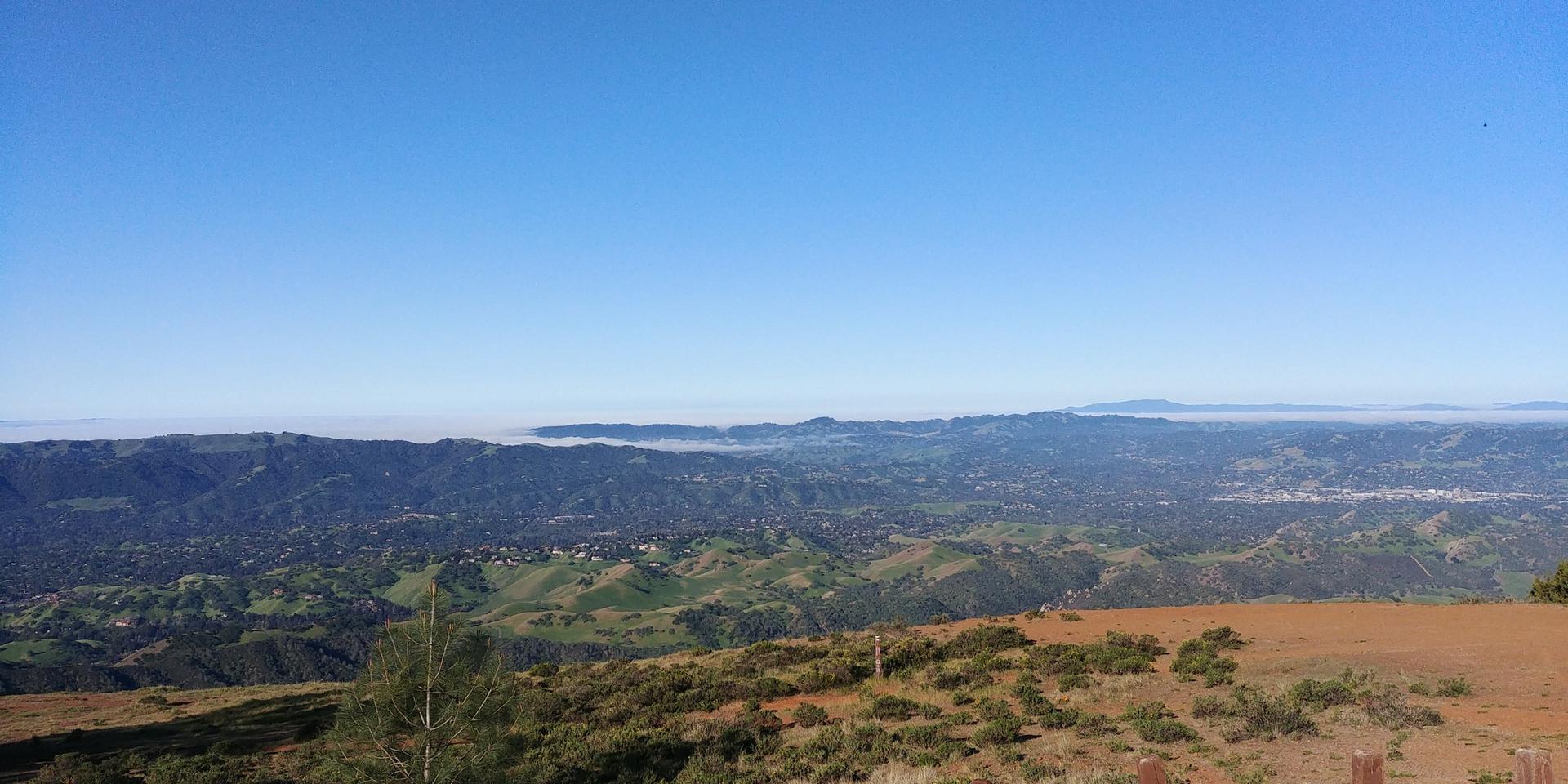 A wide view of green and brown hills stretching to a hazy distant valley.