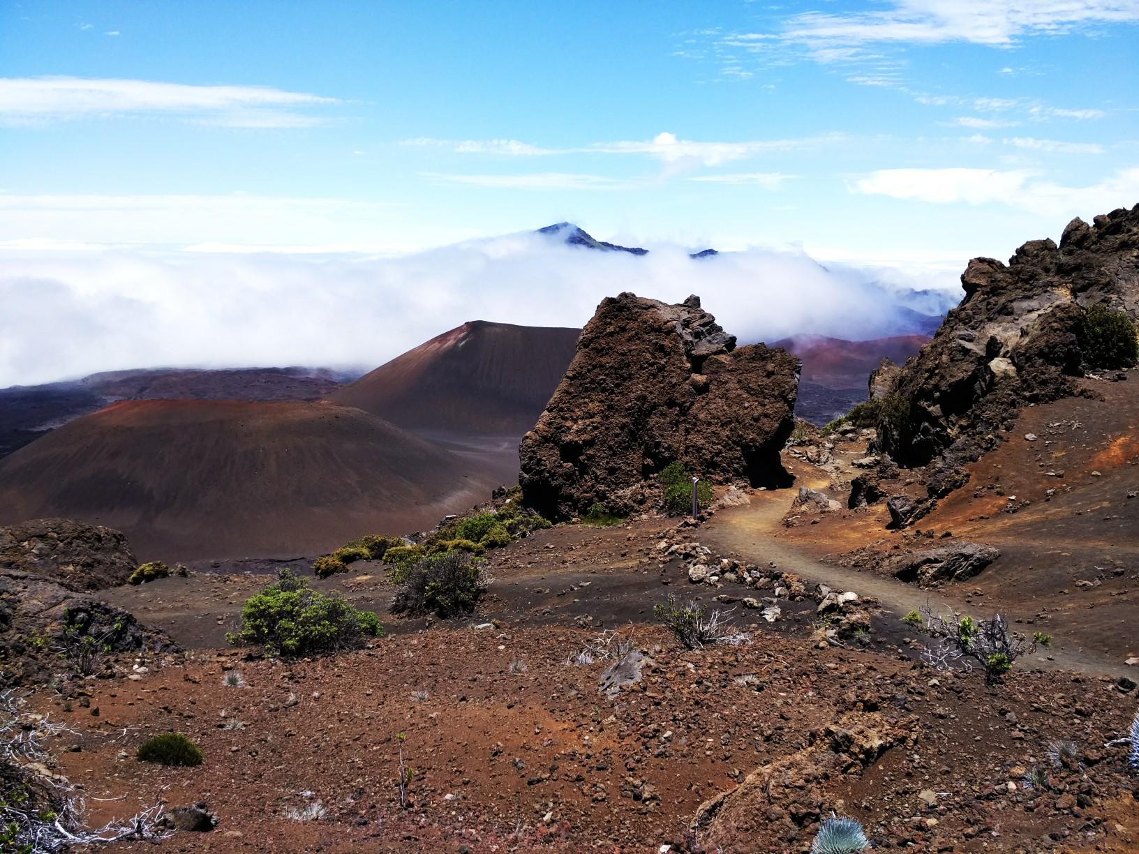 Rocky foreground with a dirt path leading to a vast volcanic landscape under clouds.