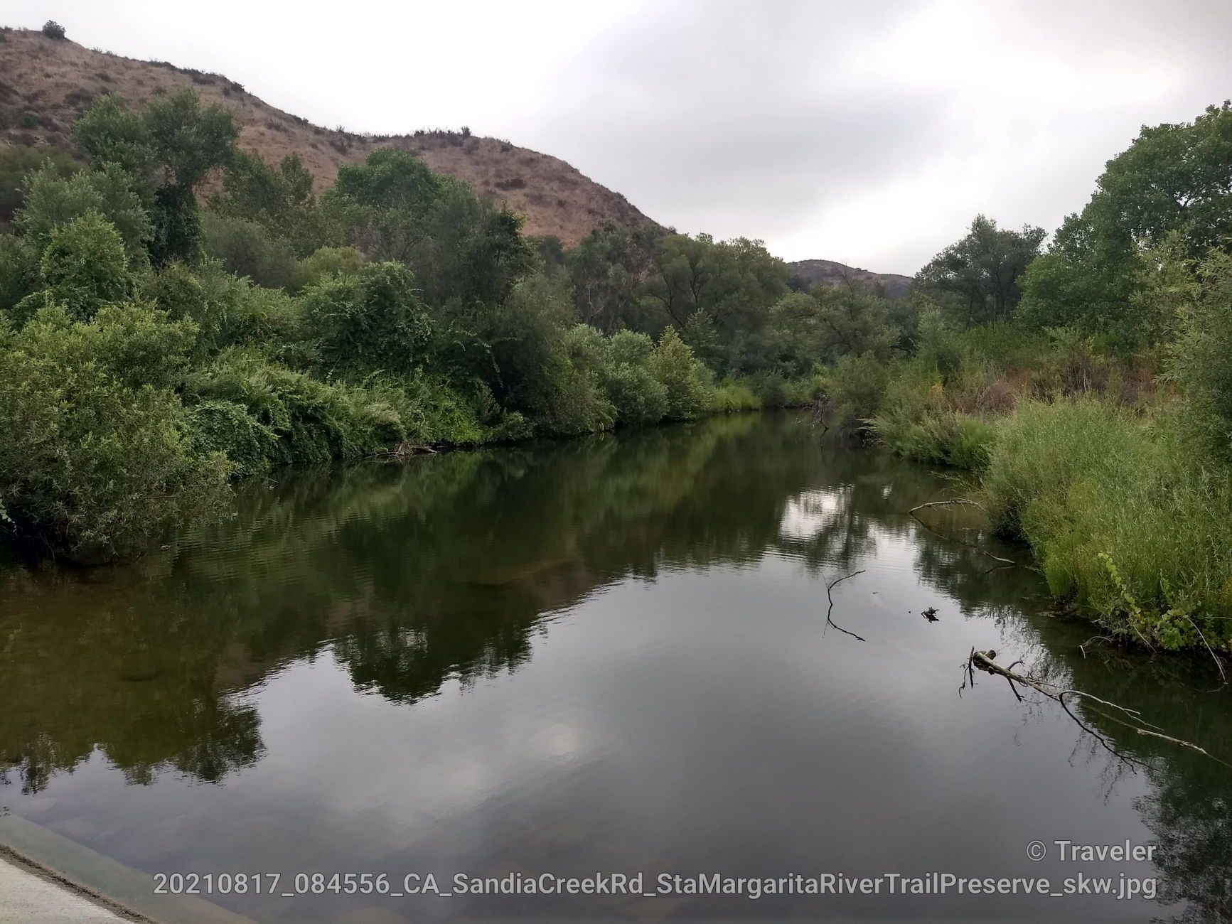 Calm river reflecting cloudy sky, flanked by lush green trees and hills. - Santa Magarita River Loop