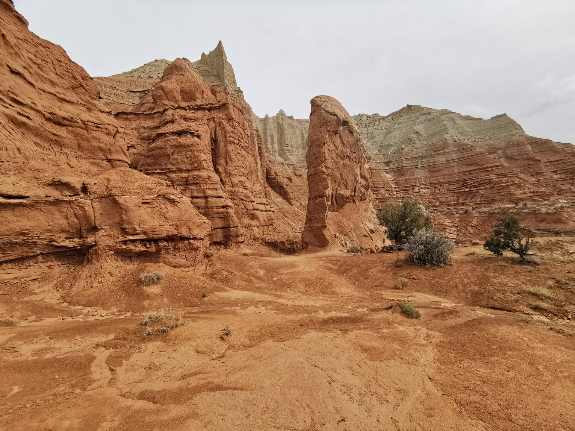 Towering red and white rock formations in a desert landscape under a cloudy sky.